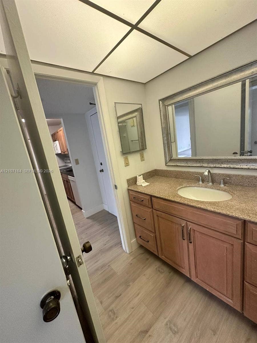 240 Lakeview Drive, #209, Weston, Weston, FL 33326 Bathroom vanity featuring wood cabinetry, stone-finish countertop with an integrated oval sink, and a wide-framed mirror, complemented by wood-finish flooring