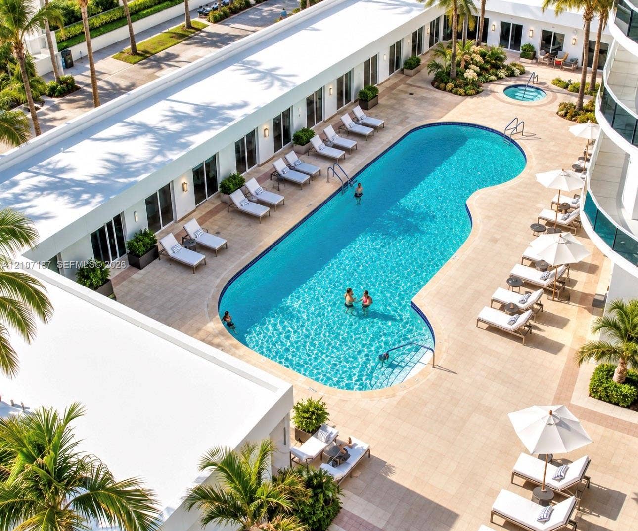9601 Collins Avenue, #403, Bal Harbour, FL 33154 Courtyard pool area featuring a curved swimming pool, integrated spa, stone-paver decking, and manicured tropical landscaping