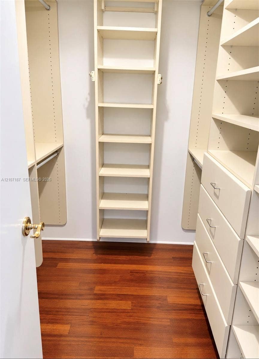 9601 Collins Avenue, #403, Bal Harbour, FL 33154 Walk-in closet featuring wood-finish flooring, custom built-in shelving, integrated hanging rods, and a multi-drawer storage unit with metallic hardware