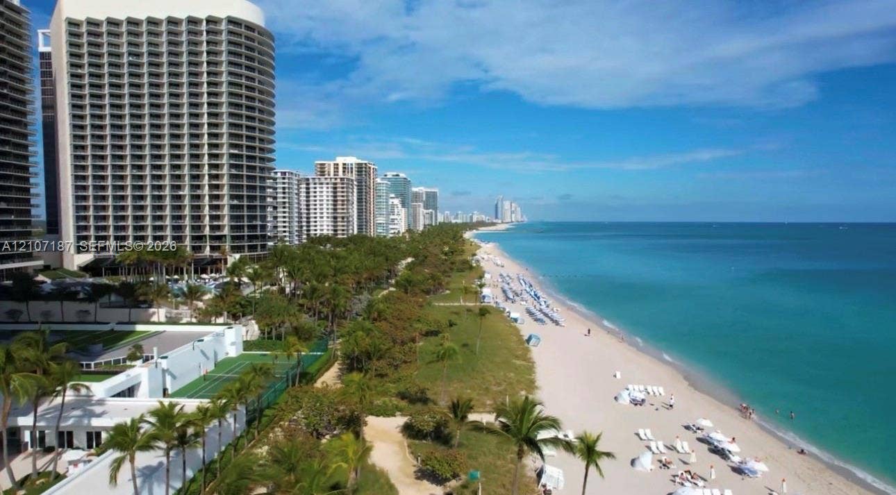 9601 Collins Avenue, #403, Bal Harbour, FL 33154 Coastal high-rise building with direct oceanfront access, featuring a private tennis court and lush palm-lined grounds situated along the sandy shoreline