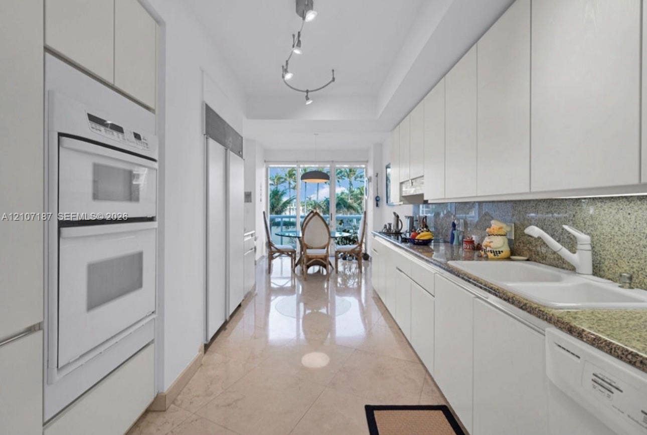 9601 Collins Avenue, #403, Bal Harbour, FL 33154 Galley kitchen featuring flat-panel cabinetry, stone countertops, double wall ovens, a dual-basin sink, and polished tile flooring