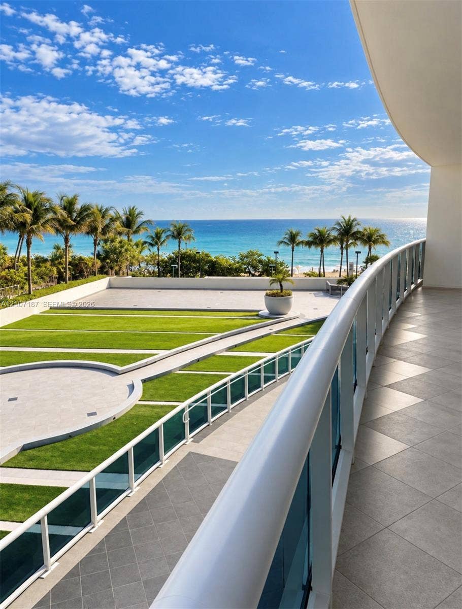 9601 Collins Avenue, #403, Bal Harbour, FL 33154 Expansive curved terrace featuring large-format stone tile flooring, a minimalist glass and white metal railing, and direct sightlines to the coastline and ocean