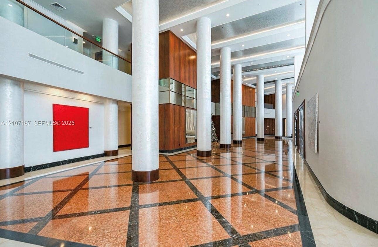 9601 Collins Avenue, #403, Bal Harbour, FL 33154 Grand atrium featuring soaring ceilings, polished stone tile flooring with geometric inlay, full-height decorative columns, and extensive wood-paneled wall accents