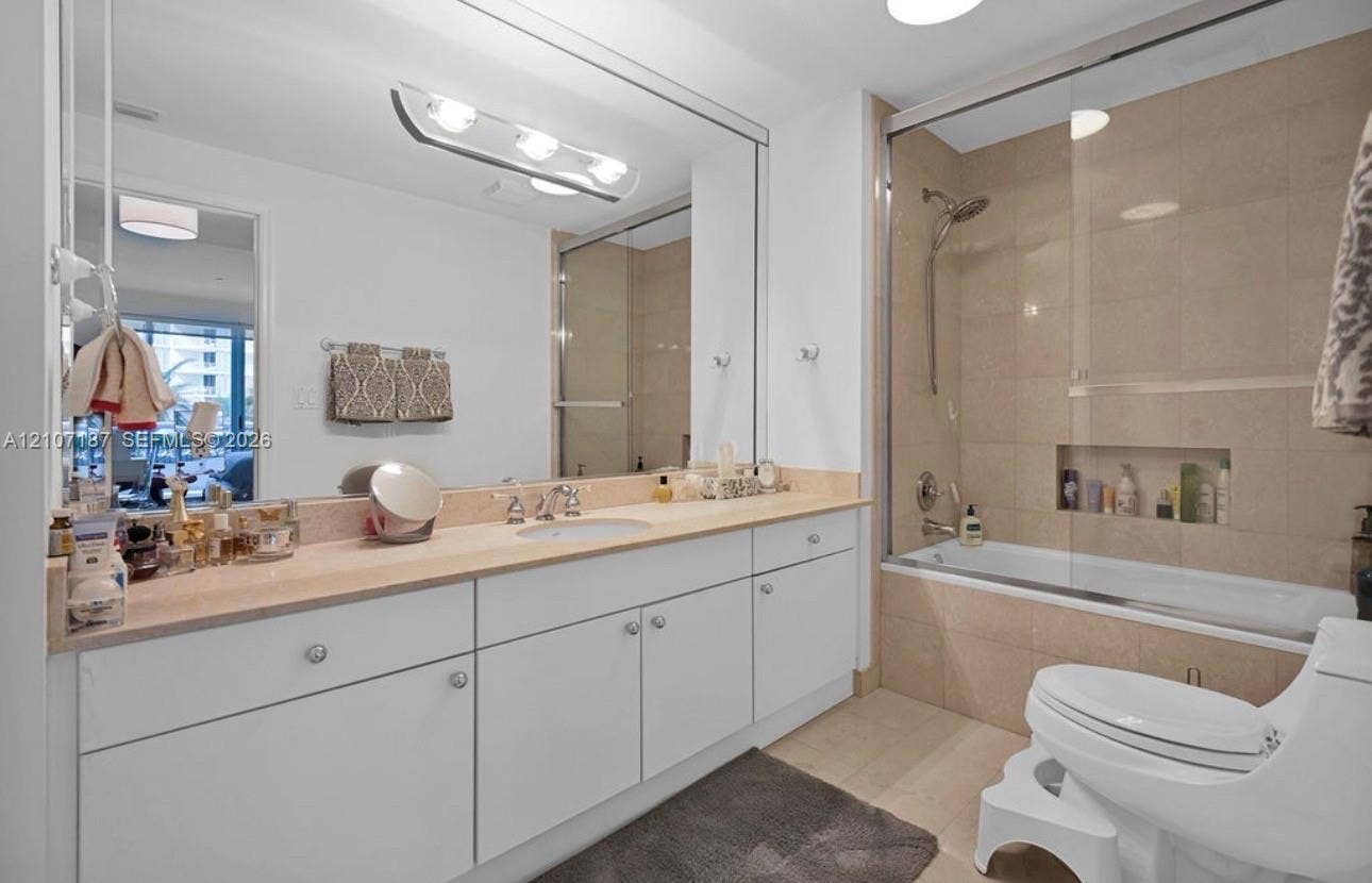 9601 Collins Avenue, #403, Bal Harbour, FL 33154 Full-width vanity with stone countertop, large-scale wall-mounted mirror, soaking tub with glass enclosure, tiled shower surround, and integrated wall niche