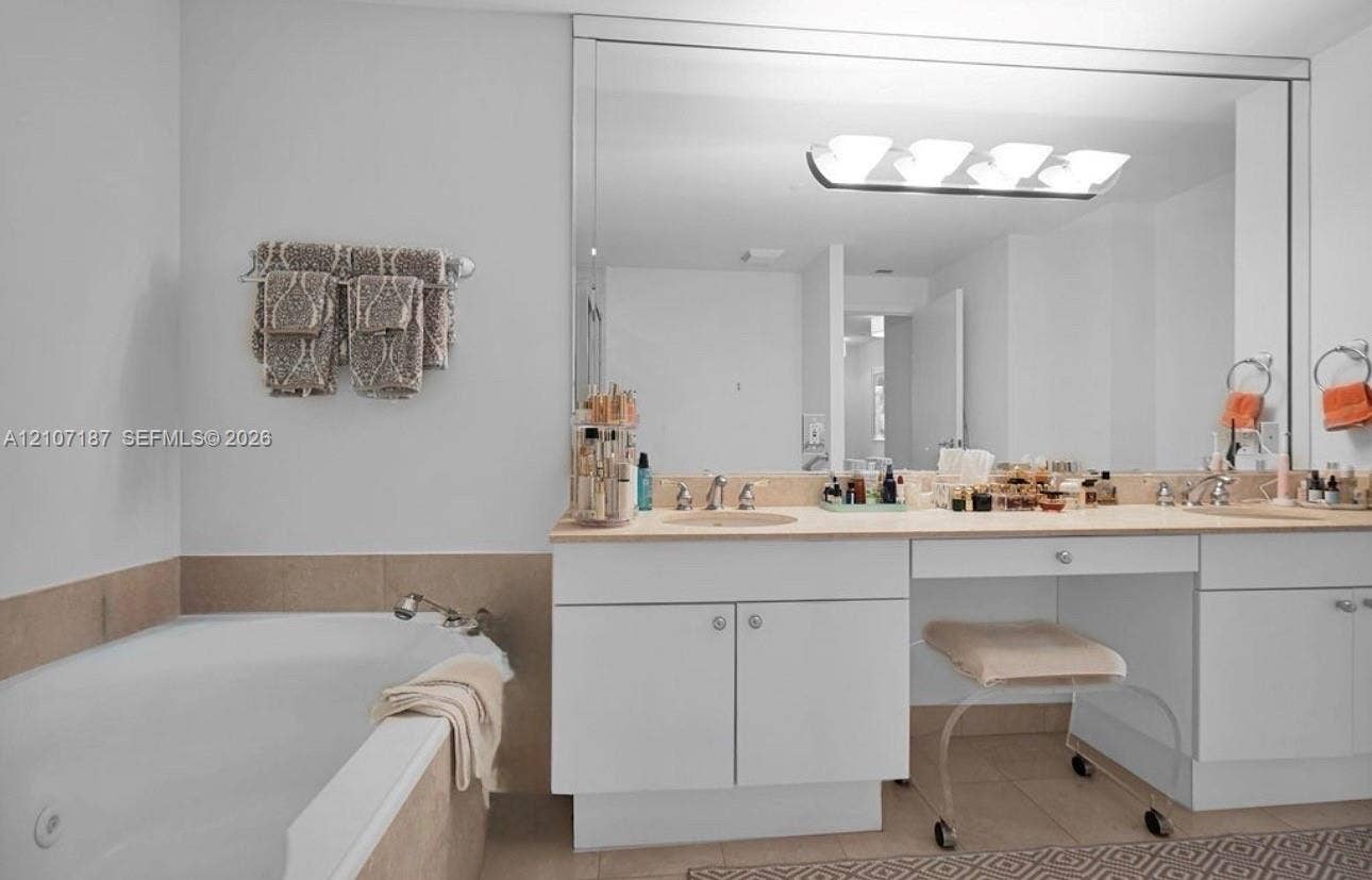 9601 Collins Avenue, #403, Bal Harbour, FL 33154 Dual-sink vanity with built-in makeup area, stone countertop, recessed lighting, and integrated full-width mirror, paired with a built-in soaking tub featuring stone tile surround