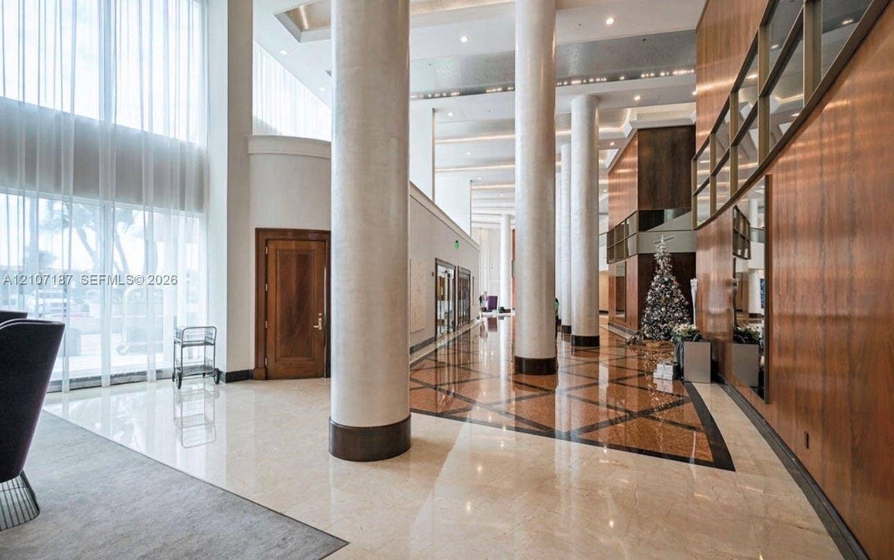 9601 Collins Avenue, #403, Bal Harbour, FL 33154 Grand lobby featuring floor-to-ceiling windows, soaring ceilings with recessed lighting, polished stone flooring with geometric tile inlay, full-height architectural columns, and wood-paneled wall accents