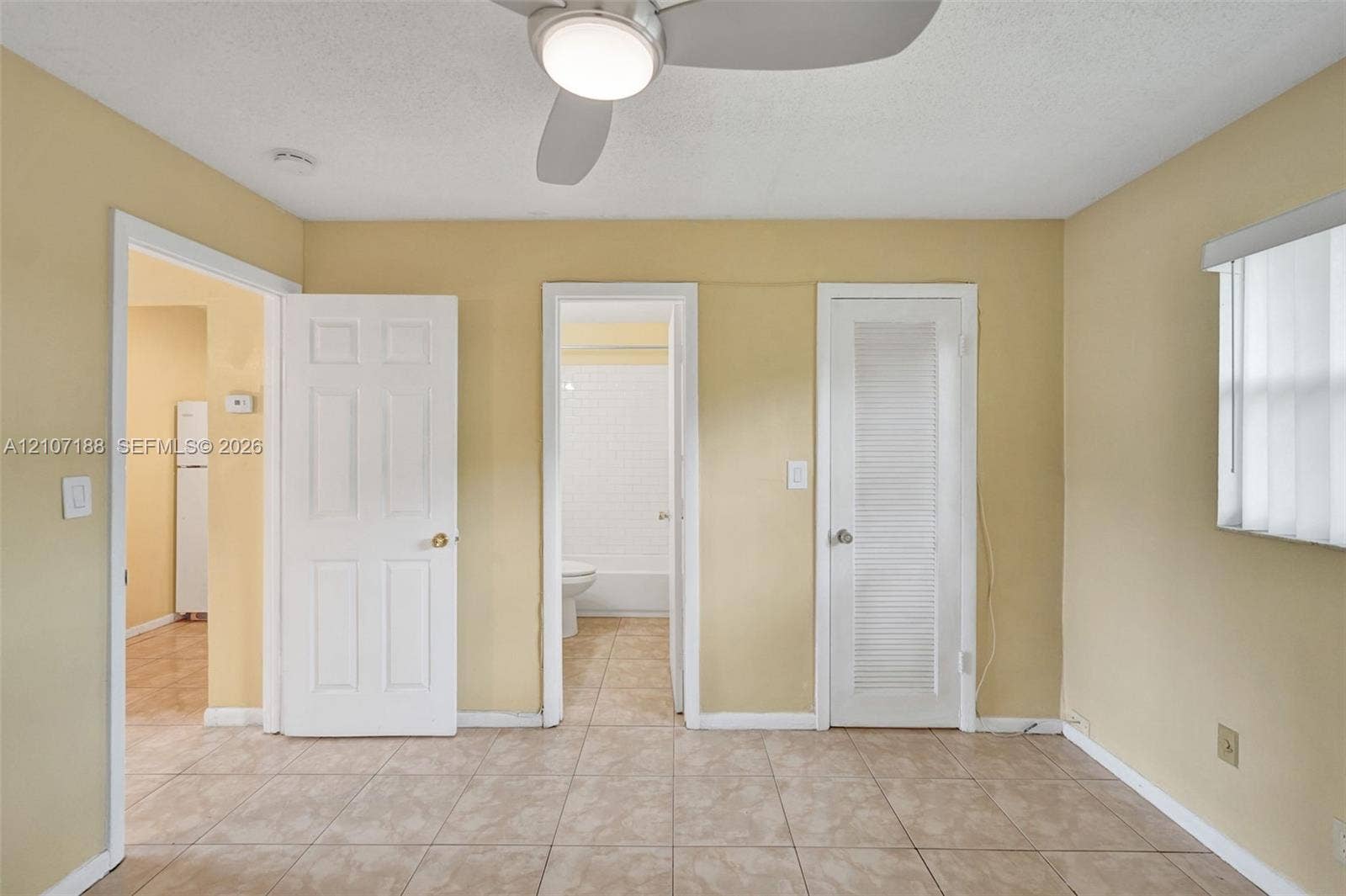 10301 NW 36th Street, #2, Coral Springs, Coral Springs, FL 33065 Neutral-toned room featuring light-colored tile flooring, a central ceiling fan with an integrated light fixture, a louvered-panel closet door, and interior paneled doors