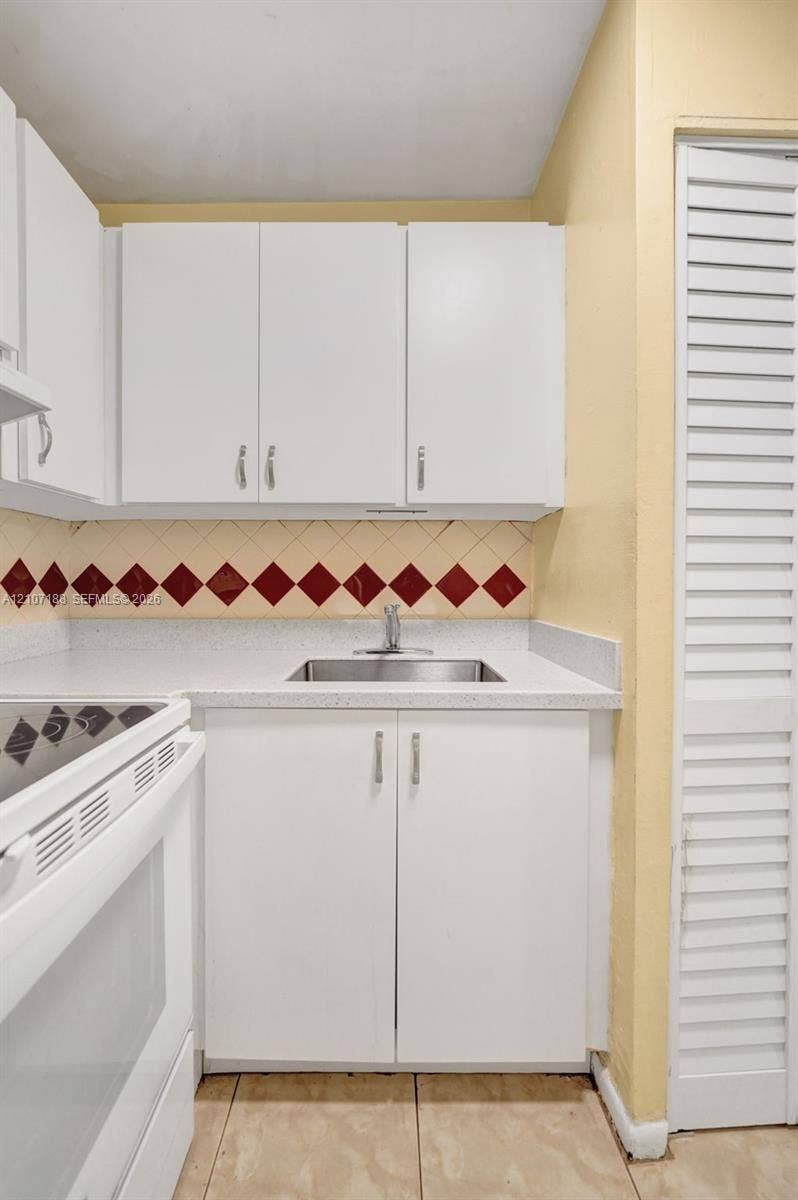 10301 NW 36th Street, #2, Coral Springs, Coral Springs, FL 33065 Kitchenette featuring white cabinetry, a neutral solid-surface countertop, stainless steel sink with a chrome faucet, diamond-patterned accent tile backsplash, and louvered closet doors