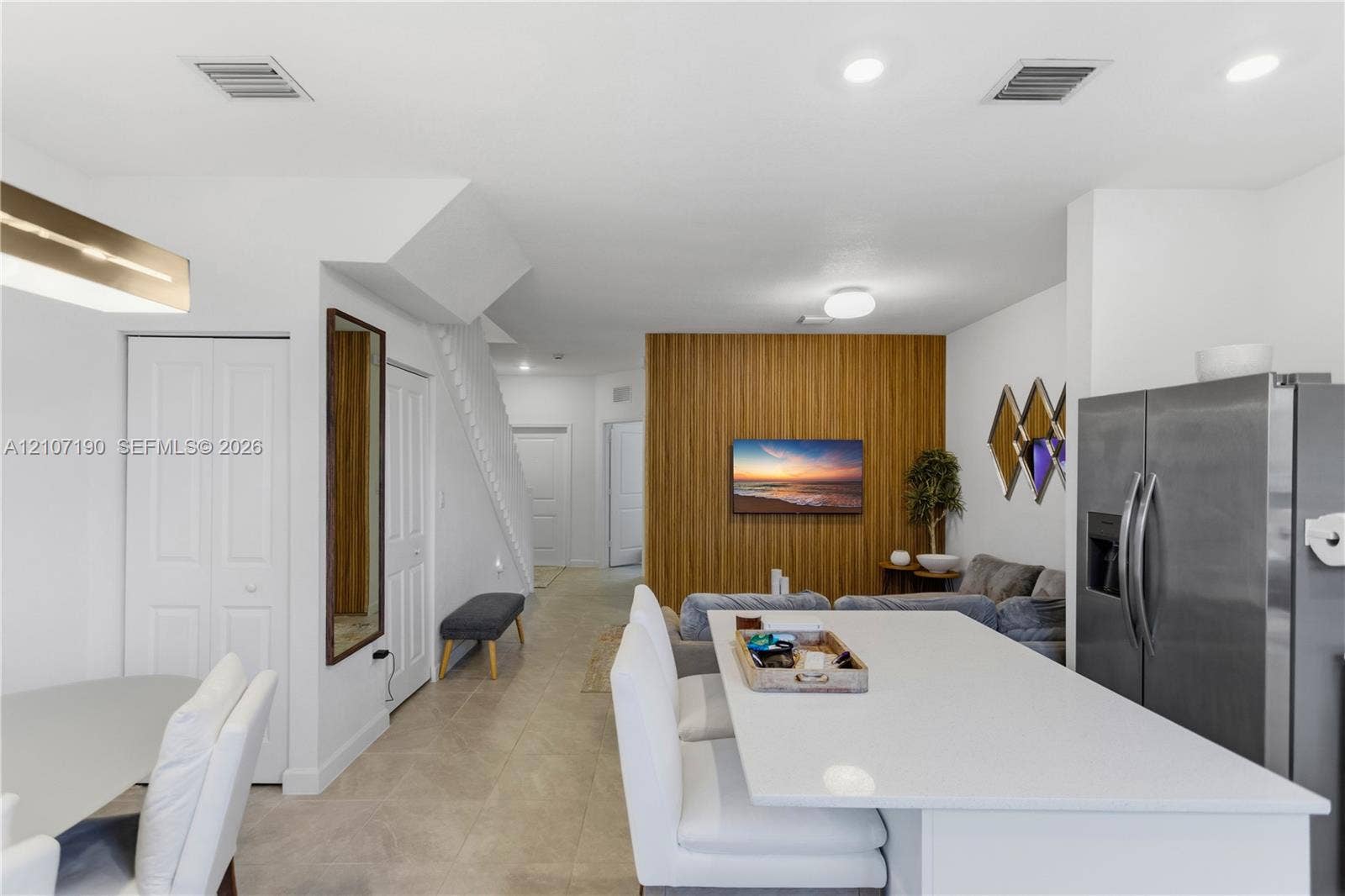 Open-concept living space featuring a central kitchen island with a neutral-toned countertop, a vertical wood-slat accent wall, tile flooring, and recessed ceiling lighting