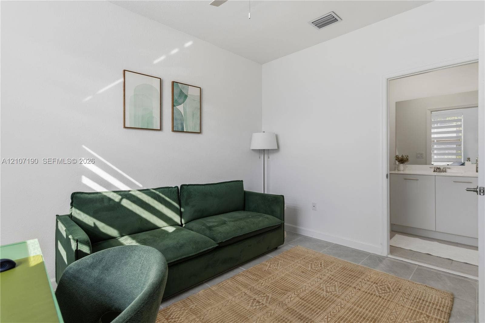 Room featuring neutral walls, gray tile flooring, and a ceiling fan, with an entrance to a bathroom containing a vanity with white cabinetry and a countertop basin