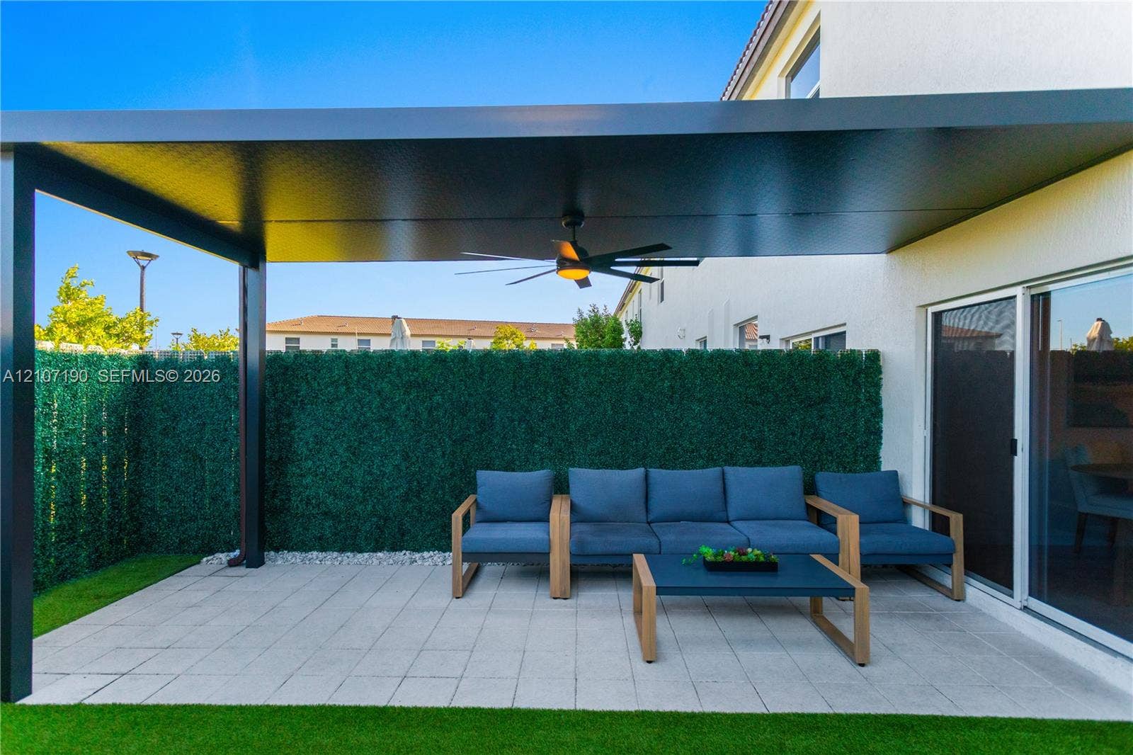 Covered patio featuring a metal pergola, ceiling fan, paver flooring, and a privacy hedge enclosure