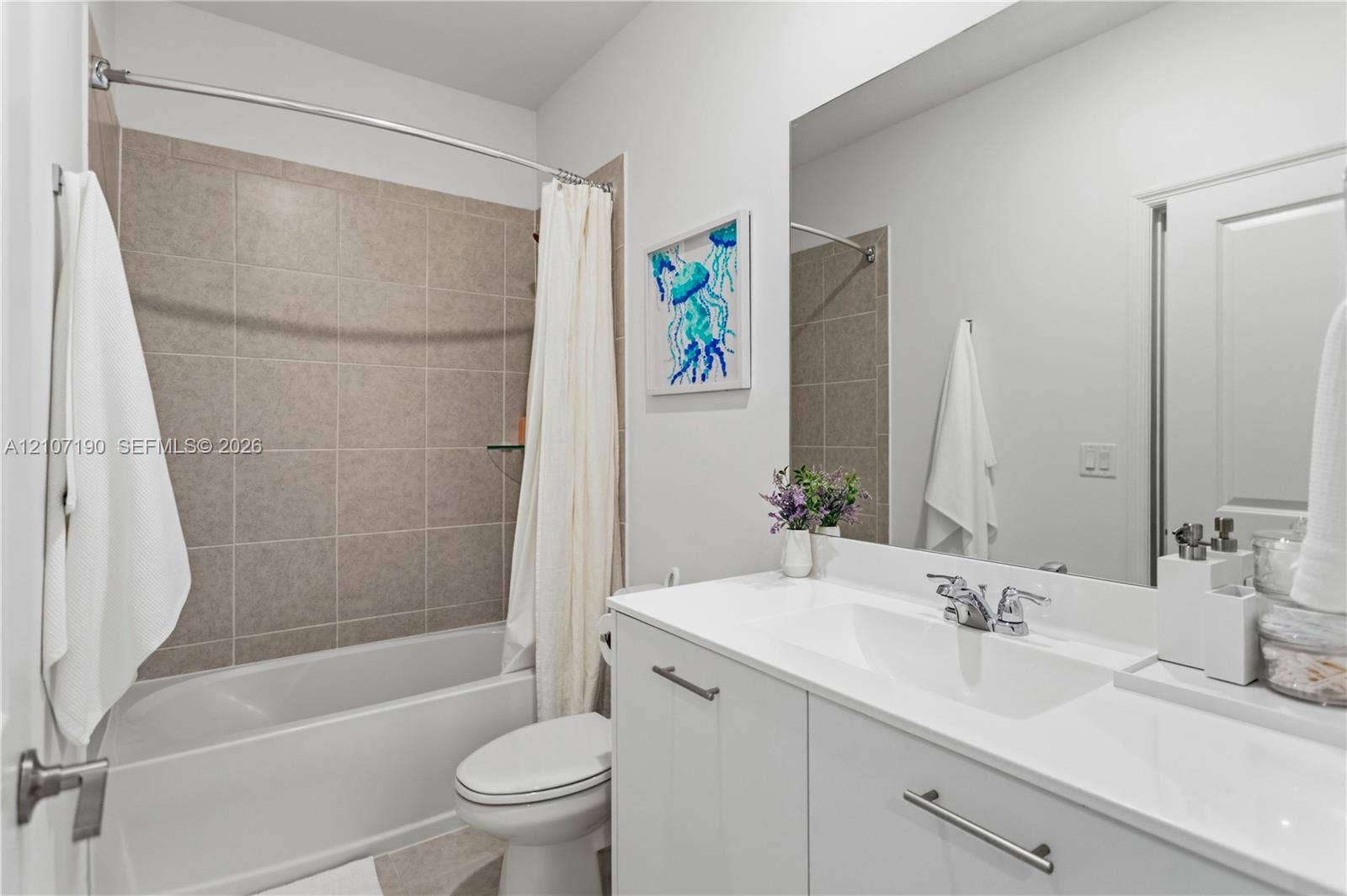 Bathroom featuring a white vanity cabinet with a solid surface countertop, an undermount sink with a polished chrome faucet, a large frameless mirror, and a tub with tiled surround