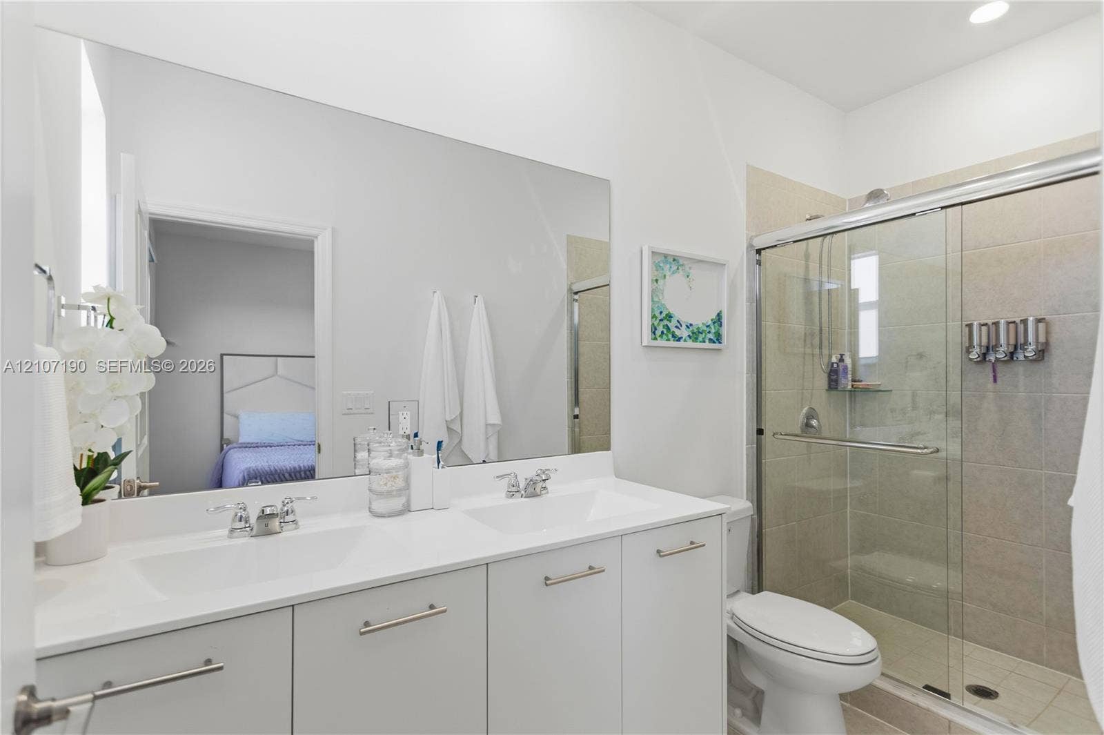 Dual-sink vanity with a white countertop and chrome fixtures, full-width vanity mirror, and a walk-in shower featuring a sliding glass door and tile wall surround