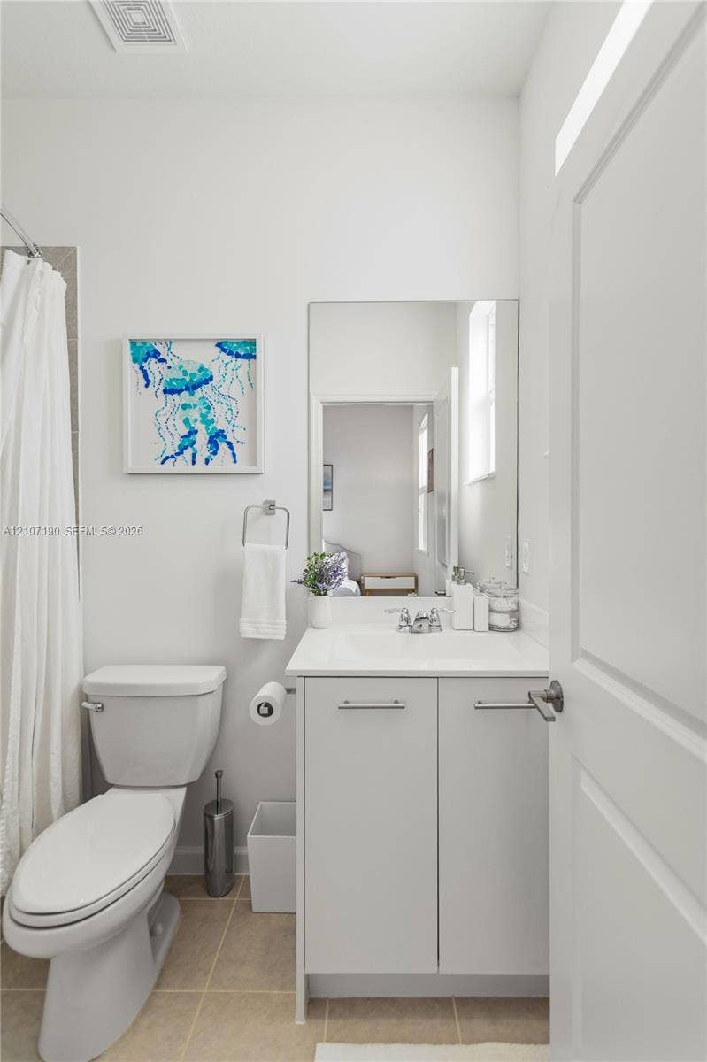 Bathroom featuring a white cabinet vanity with a countertop sink, chrome hardware, a rectangular wall-mounted mirror, and tile flooring