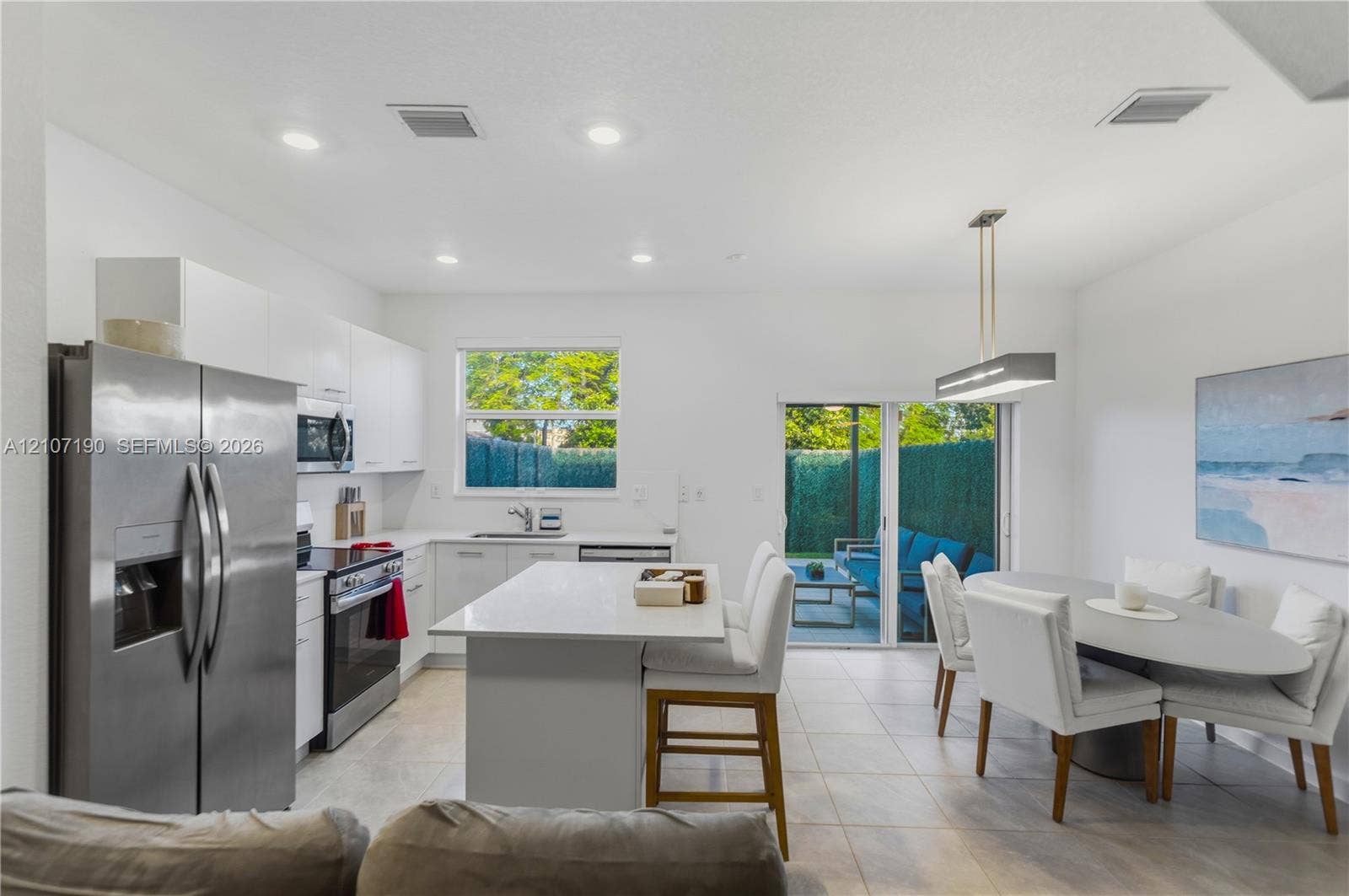 Kitchen featuring white flat-panel cabinetry, central island with stone-surface countertop, stainless steel appliances, recessed ceiling lighting, and large-format tile flooring