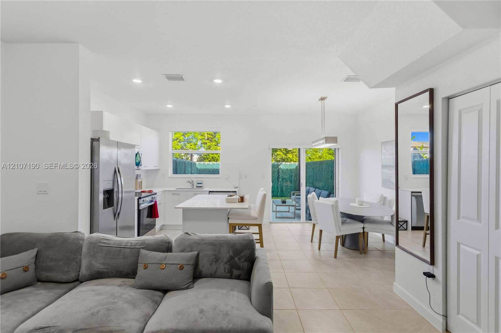 Kitchen featuring white flat-panel cabinetry, a central island with a solid-surface countertop, stainless steel appliances, recessed ceiling lighting, and large-format tile flooring
