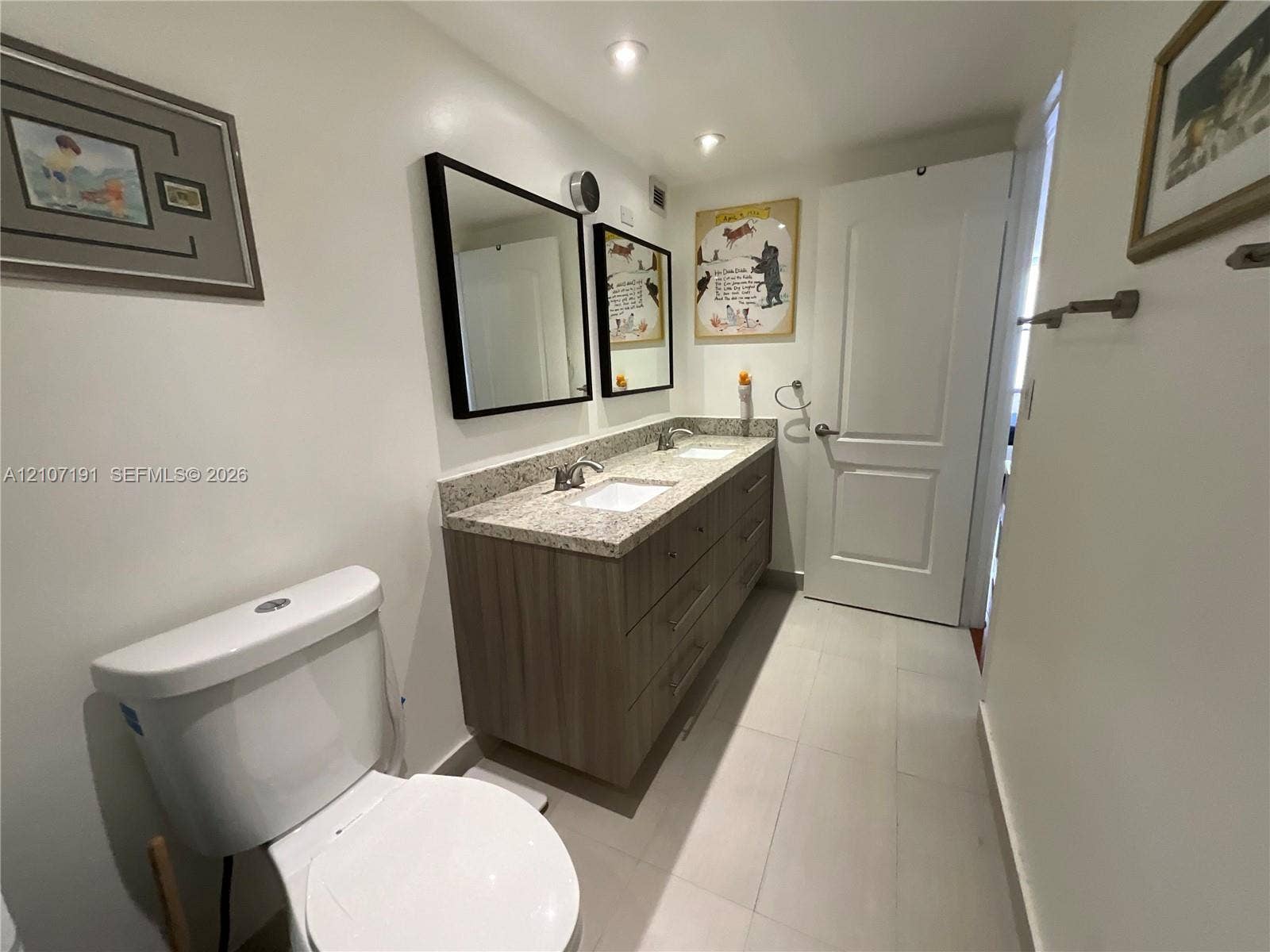Dual-sink vanity featuring stone-finish countertops, wood-finish cabinetry, rectangular under-mount basins, and two framed wall mirrors