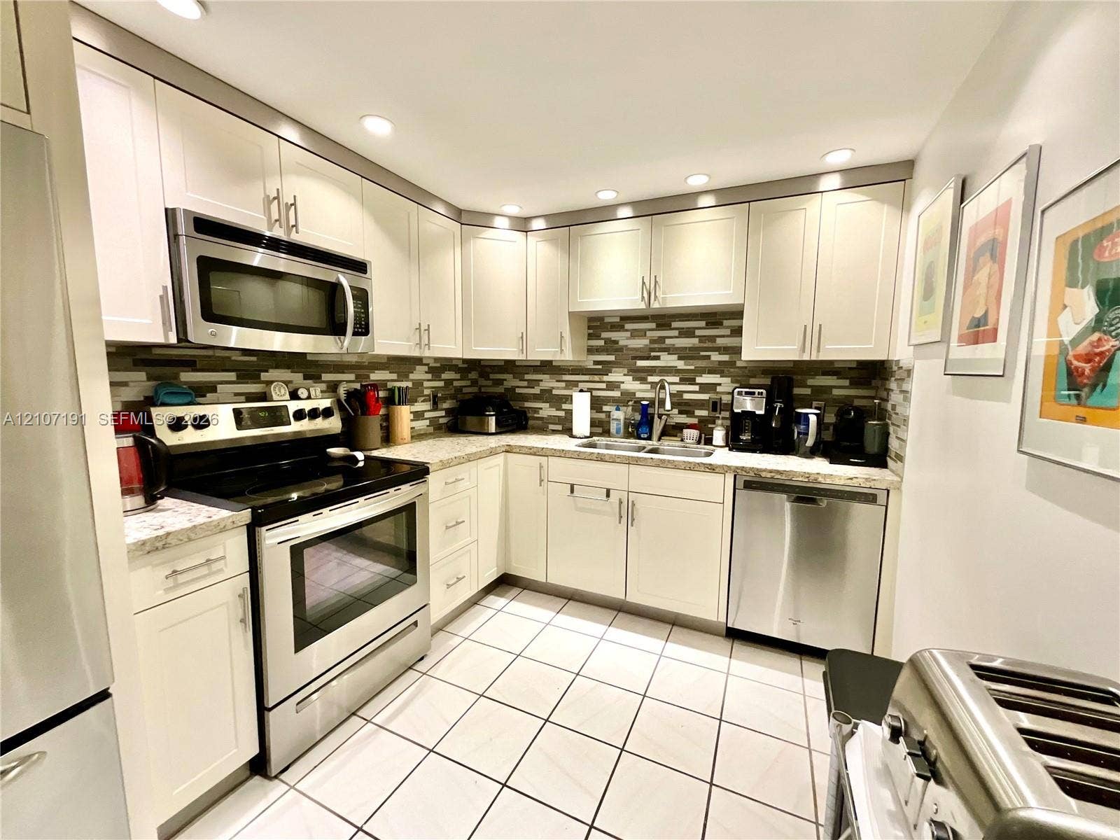 Kitchen featuring shaker-style cabinetry, stainless steel appliances, speckled stone-finish countertops, decorative multi-tone tile backsplash, and recessed lighting