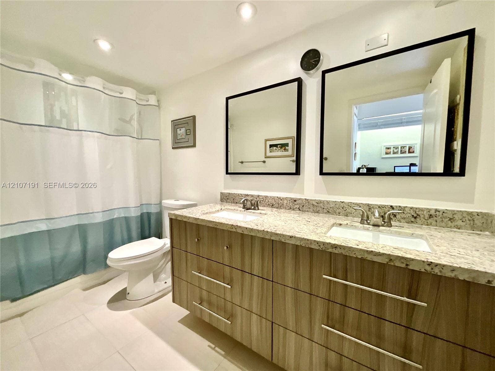 Dual-sink vanity with wood-finish cabinetry, stone countertop, two framed mirrors, and recessed lighting