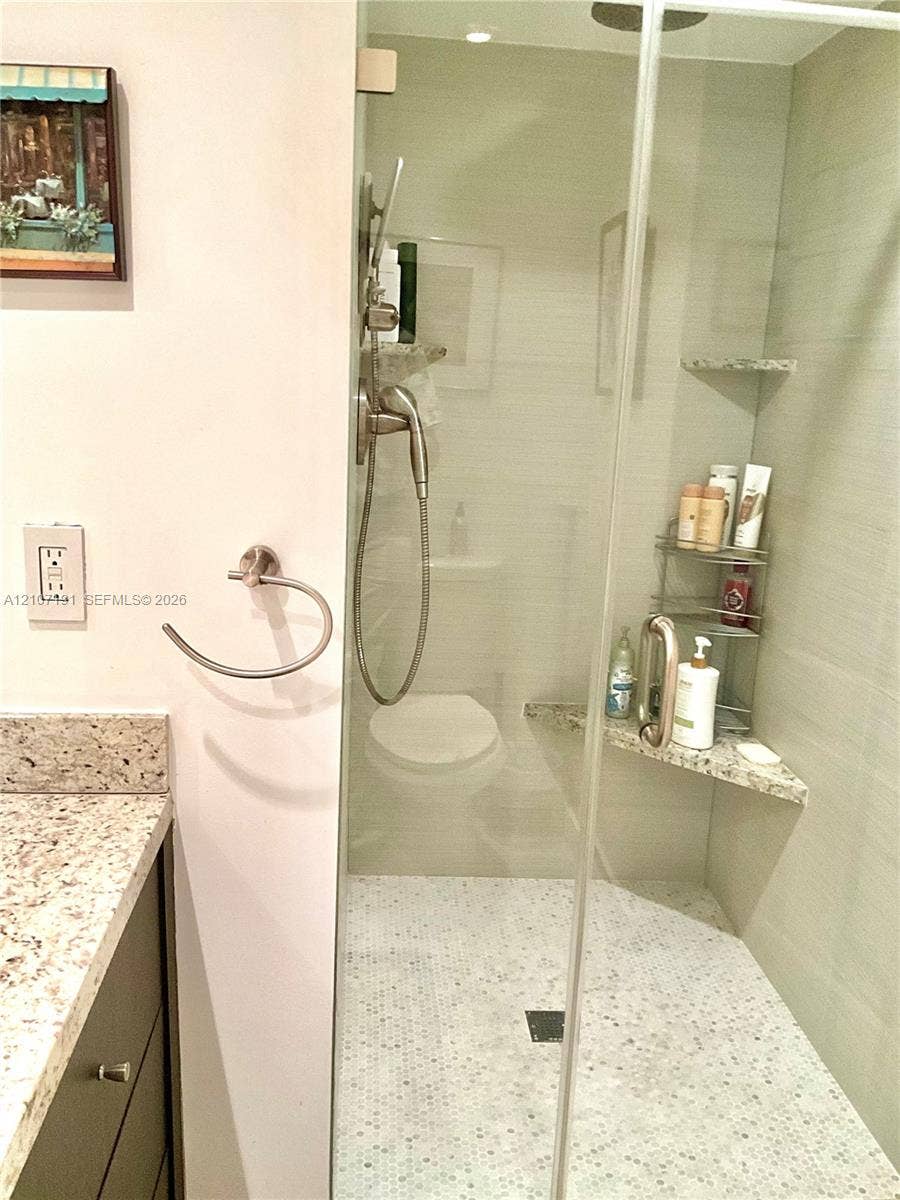 Walk-in shower featuring a frameless glass door, stone tile surround, integrated corner bench, and small-format hexagonal floor tile, complemented by a vanity with a stone countertop