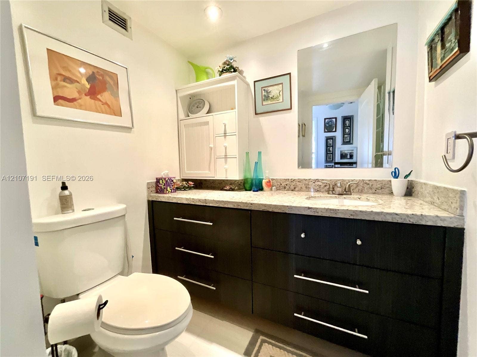 Dark-toned vanity with integrated cabinetry, speckled stone-finish countertop, undermount sink, and recessed wall-mounted mirror
