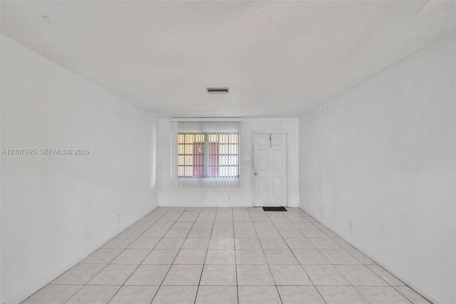 10301 NW 36th Street, #5, Coral Springs, Coral Springs, FL 33065 Spacious room featuring neutral tile flooring, smooth white walls, vertical window blinds, and a paneled entry door