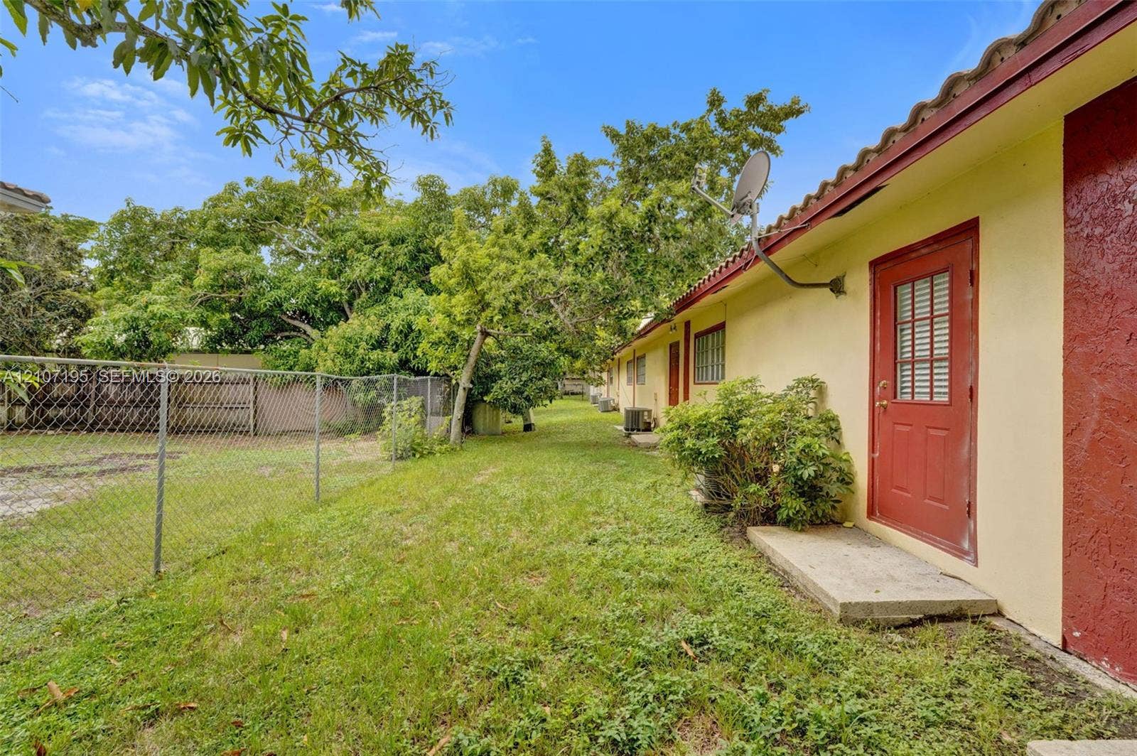 10301 NW 36th Street, #5, Coral Springs, Coral Springs, FL 33065 Exterior side yard featuring a chain-link perimeter fence, mature trees, concrete door step, and a red door with integrated window panels