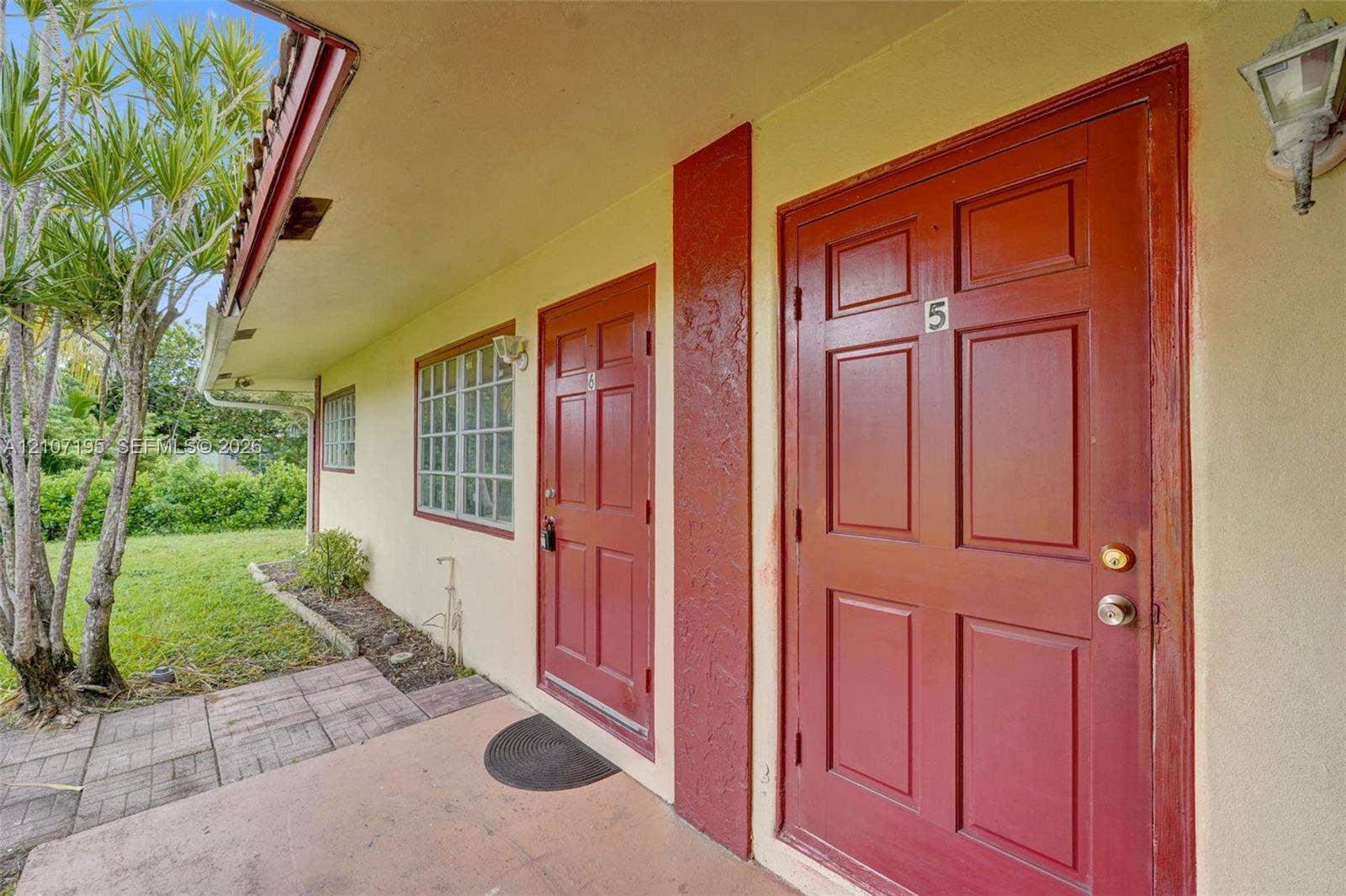 10301 NW 36th Street, #5, Coral Springs, Coral Springs, FL 33065 Exterior walkway featuring a concrete patio, six-panel solid core doors, glass block windows, and wall-mounted exterior light fixtures