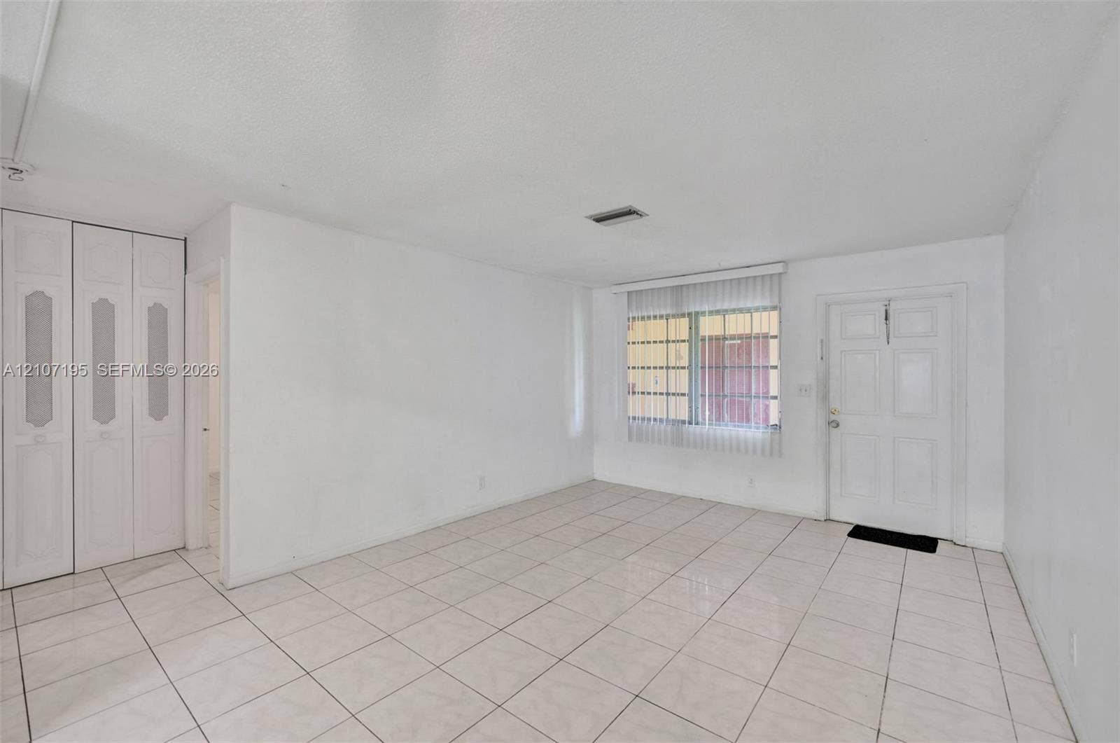 10301 NW 36th Street, #5, Coral Springs, Coral Springs, FL 33065 Living area featuring light-toned tile flooring, built-in floor-to-ceiling closet cabinetry, a multi-pane window with vertical blinds, and a paneled entry door