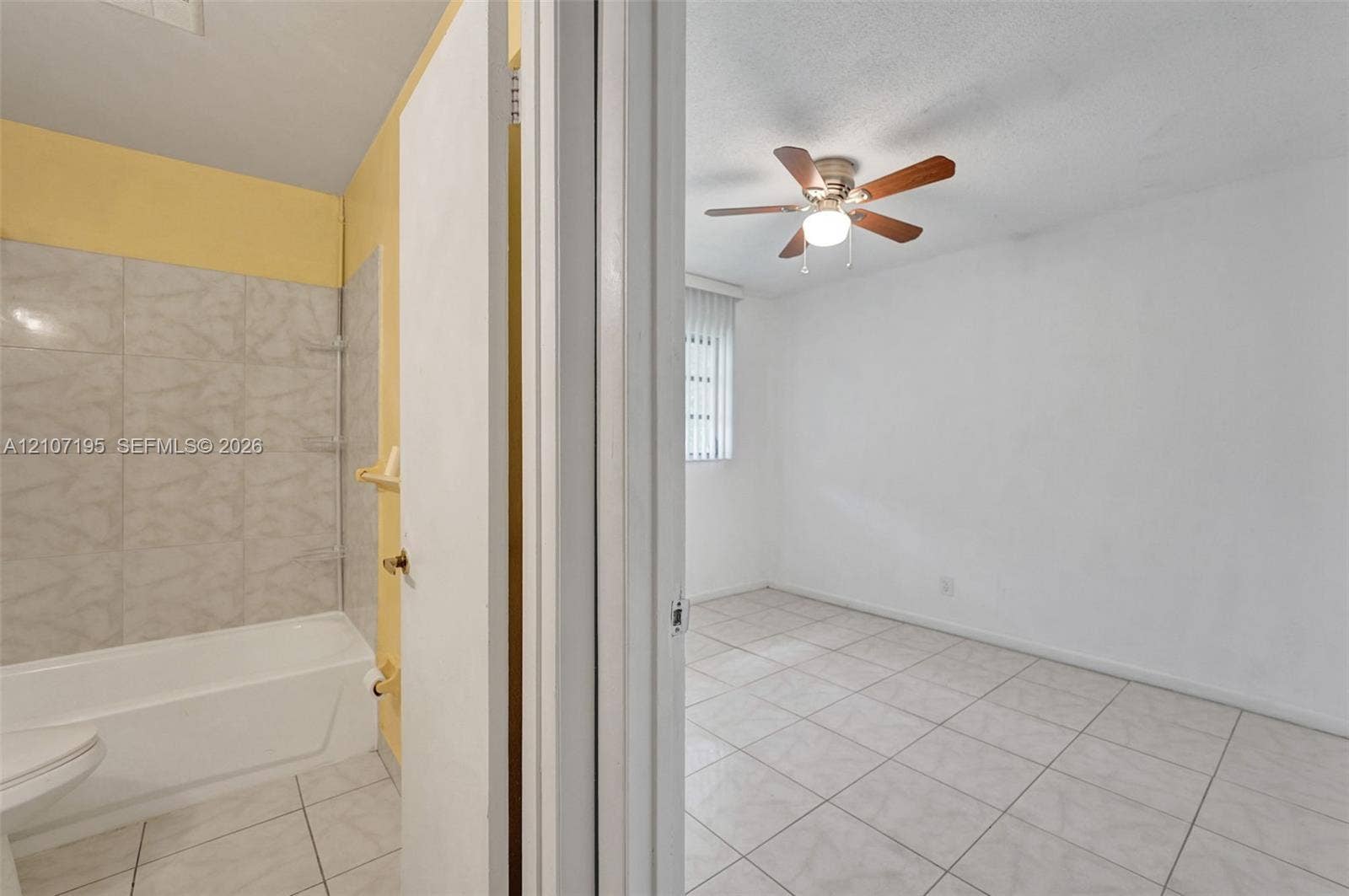 10301 NW 36th Street, #5, Coral Springs, Coral Springs, FL 33065 Bathroom featuring a tile-surround bathtub and neutral wall finishes, paired with an interior space highlighted by ceramic tile flooring, a ceiling fan with integrated lighting, and a vertical blind window treatment