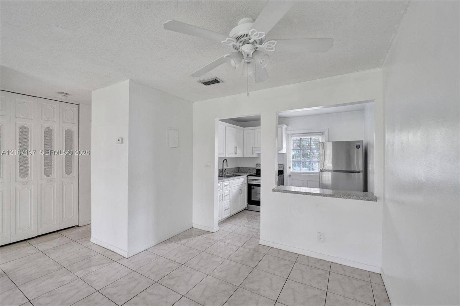 10301 NW 36th Street, #6, Coral Springs, Coral Springs, FL 33065 Tiled flooring, ceiling fan with light fixture, floor-to-ceiling bi-fold closet doors, and pass-through window with a stone-finish countertop