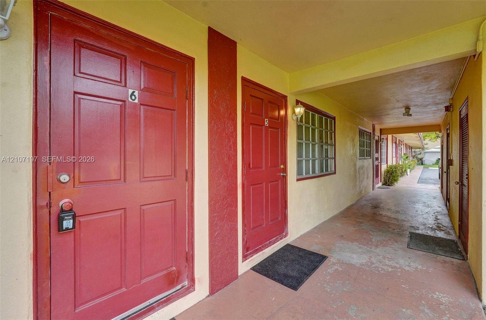 10301 NW 36th Street, #6, Coral Springs, Coral Springs, FL 33065 Covered exterior corridor featuring painted paneled doors, wall-mounted light fixtures, and multi-pane grid windows