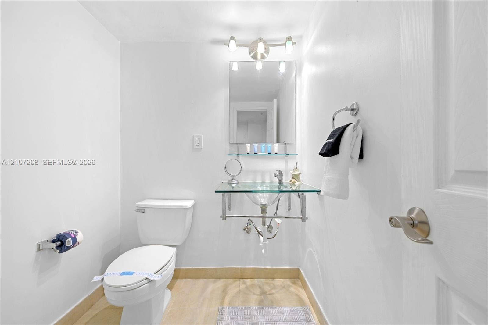 19370 Collins Avenue, #1405, Sunny Isles Beach, Sunny Isles Beach, FL 33160 Glass-top wall-mounted sink with chrome hardware, rectangular mirror, glass shelf, three-light vanity fixture, and porcelain-finish flooring