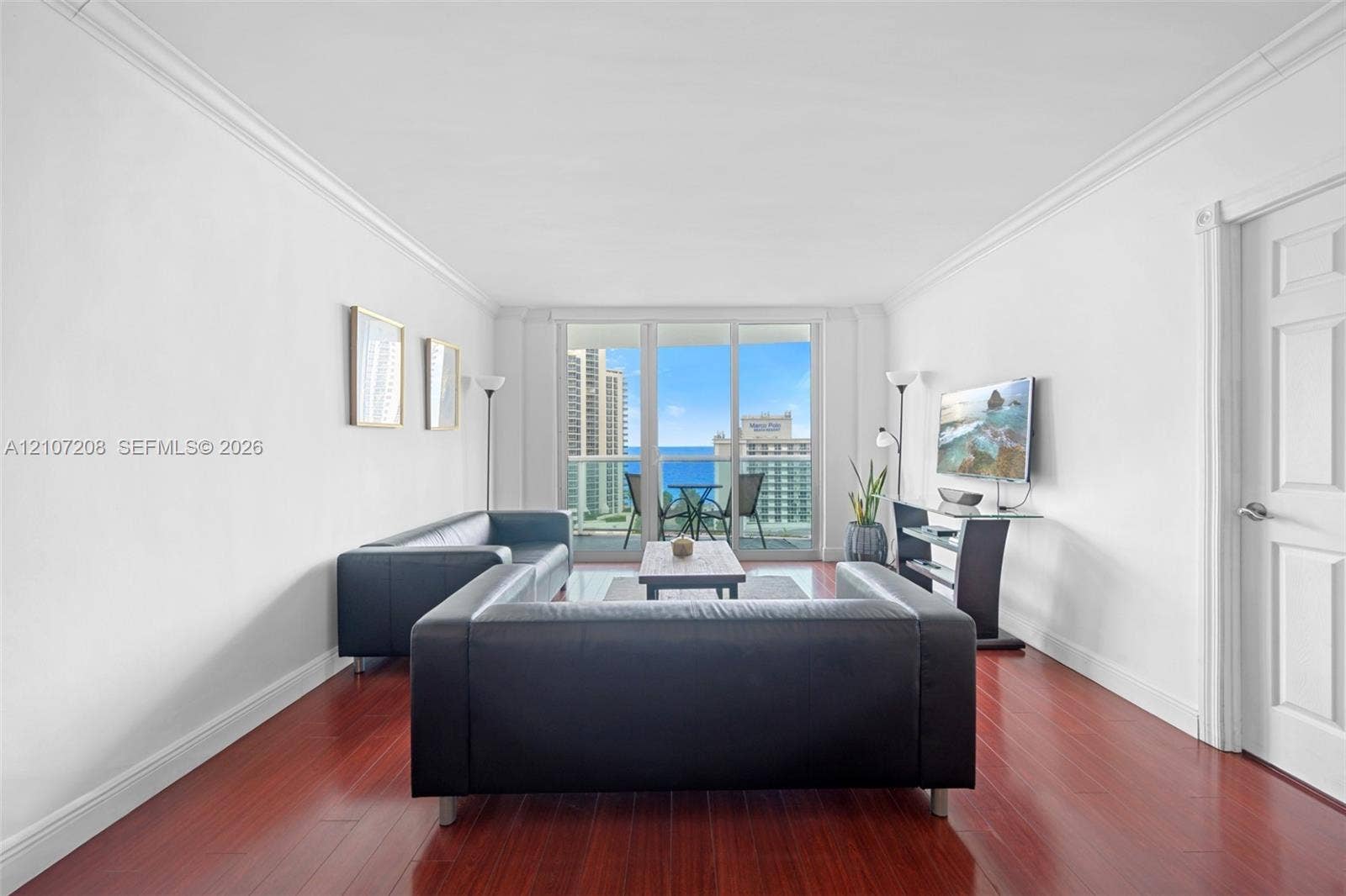 19370 Collins Avenue, #1405, Sunny Isles Beach, Sunny Isles Beach, FL 33160 Interior space featuring wood-finish flooring, crown molding, and floor-to-ceiling glass panel sliding doors opening to an exterior balcony