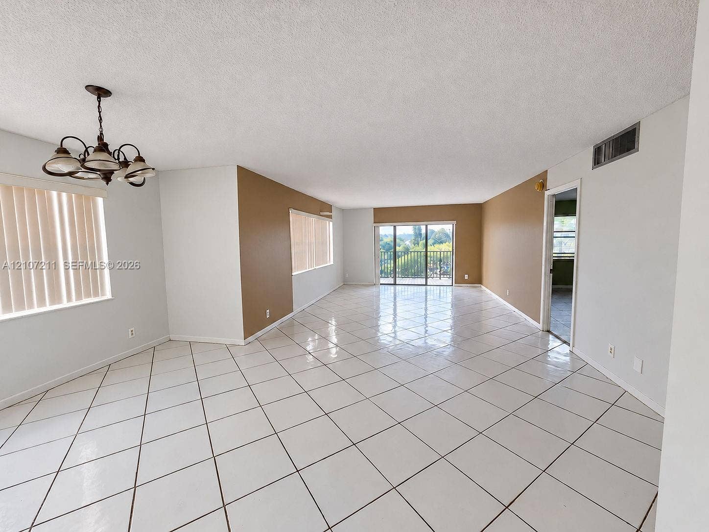 Spacious room featuring white ceramic tile. Wall paint digitally enhanced using AI.flooring, neutral wall tones, a multi-arm chandelier, and sliding glass doors leading to a balcony
