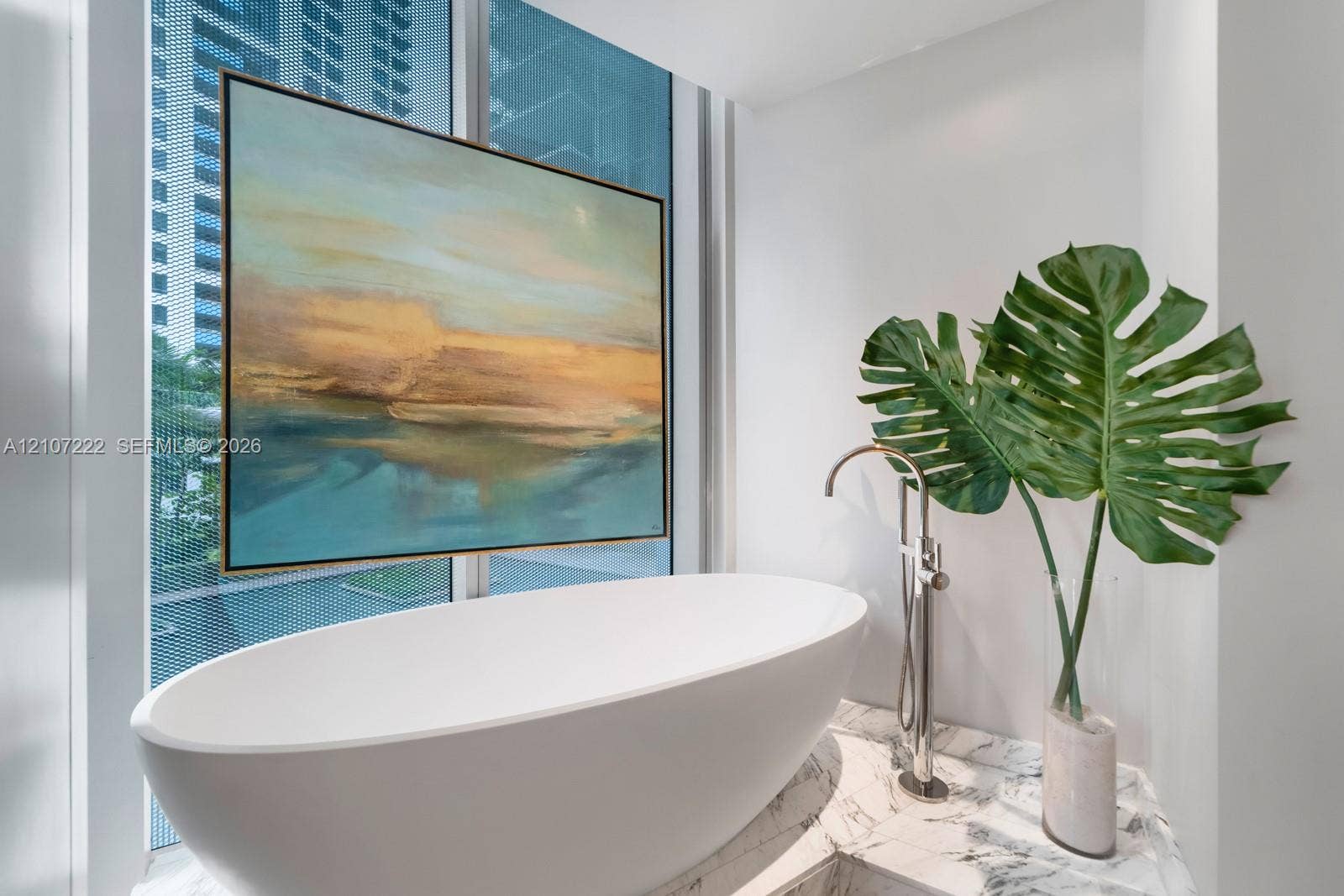 1300 Monad Terrace, #2F, Miami Beach, FL 33139 Freestanding white soaking tub with a floor-mounted metallic faucet, situated atop a stone-surfaced platform and flanked by floor-to-ceiling windows