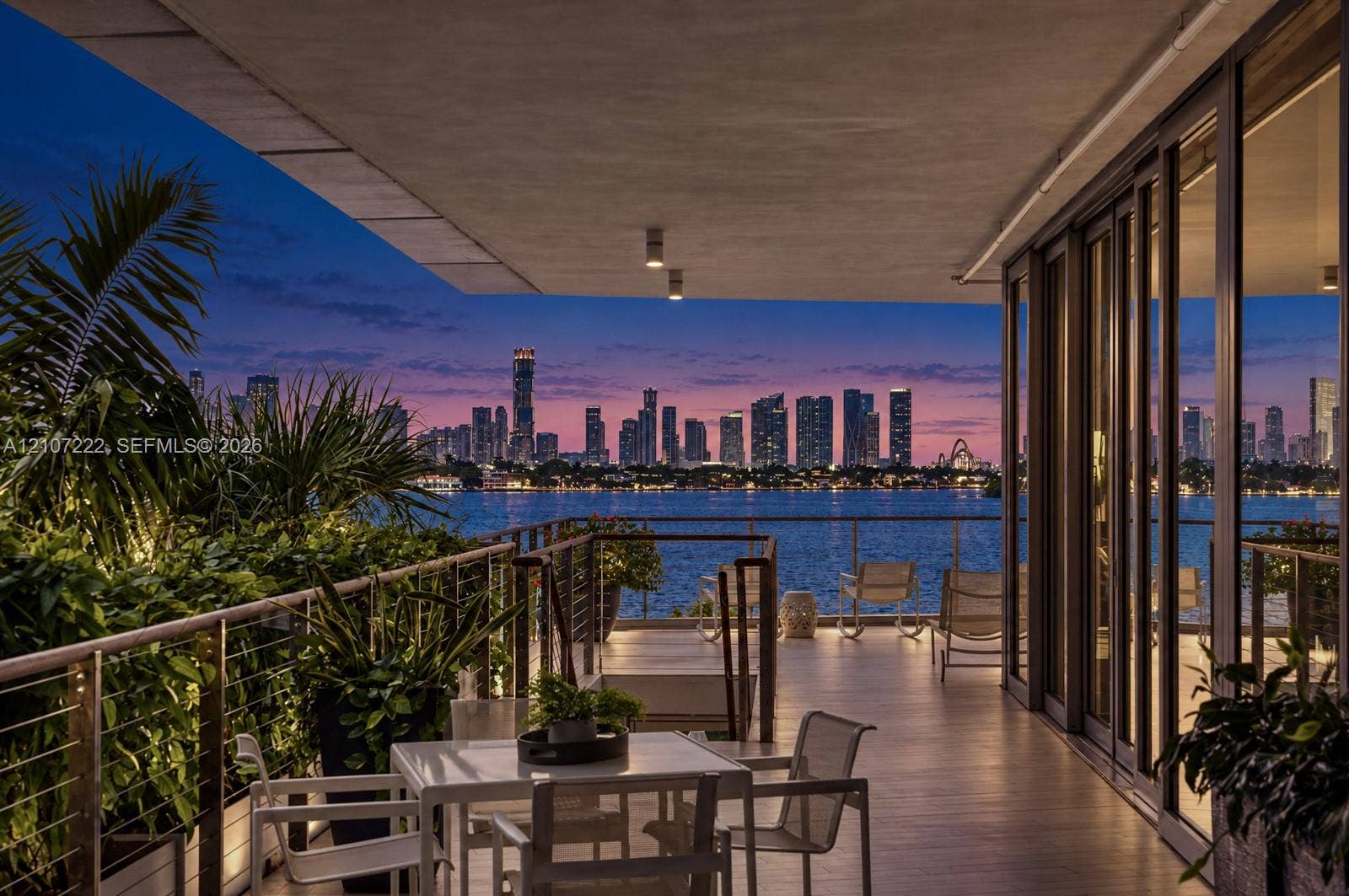 1300 Monad Terrace, #2F, Miami Beach, FL 33139 Expansive covered terrace featuring floor-to-ceiling glass walls, integrated ceiling lighting, and a metal cable railing system overlooking the water and city skyline