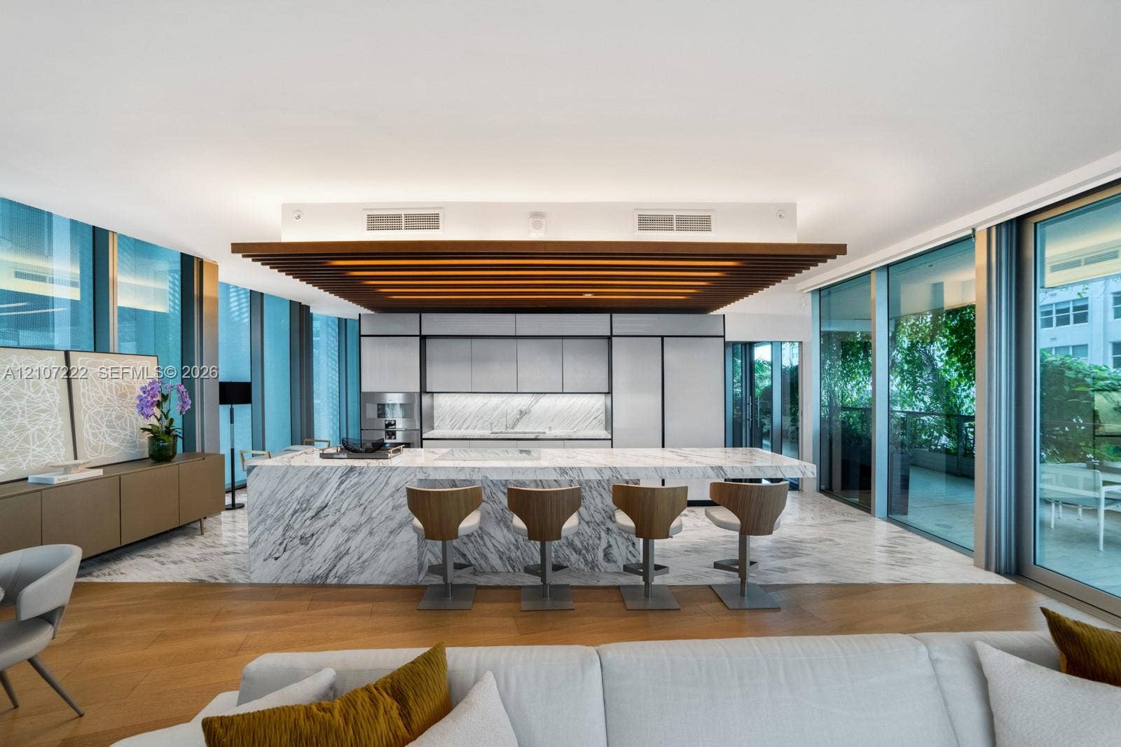 1300 Monad Terrace, #2F, Miami Beach, FL 33139 Kitchen featuring an expansive stone-topped island with integrated seating, stone flooring, floor-to-ceiling glass panel walls, and custom wood-slat ceiling detail