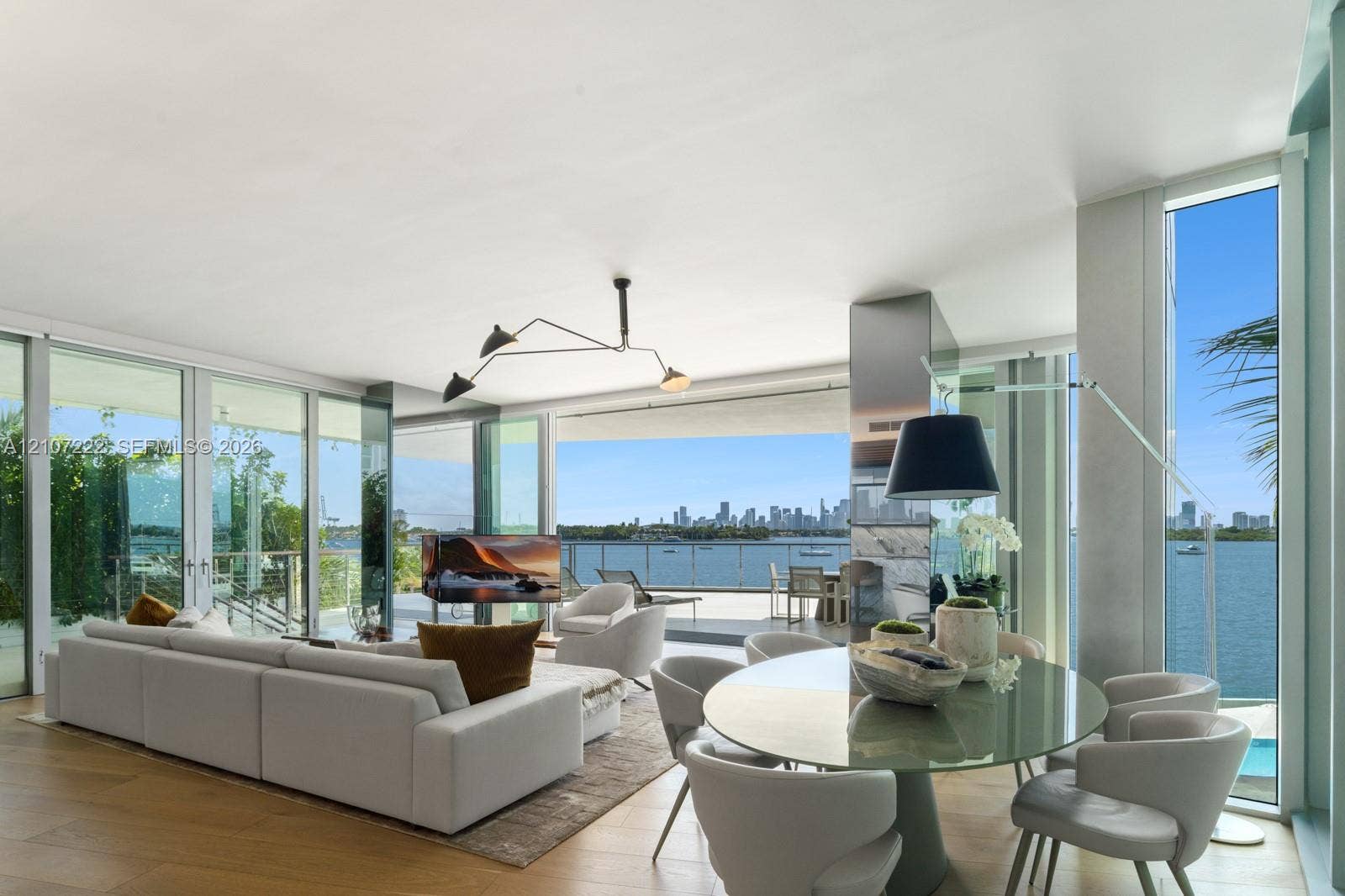 1300 Monad Terrace, #2F, Miami Beach, FL 33139 Floor-to-ceiling glass walls, wood-finish flooring, recessed architectural lighting, and a large private balcony with water and city skyline scenery
