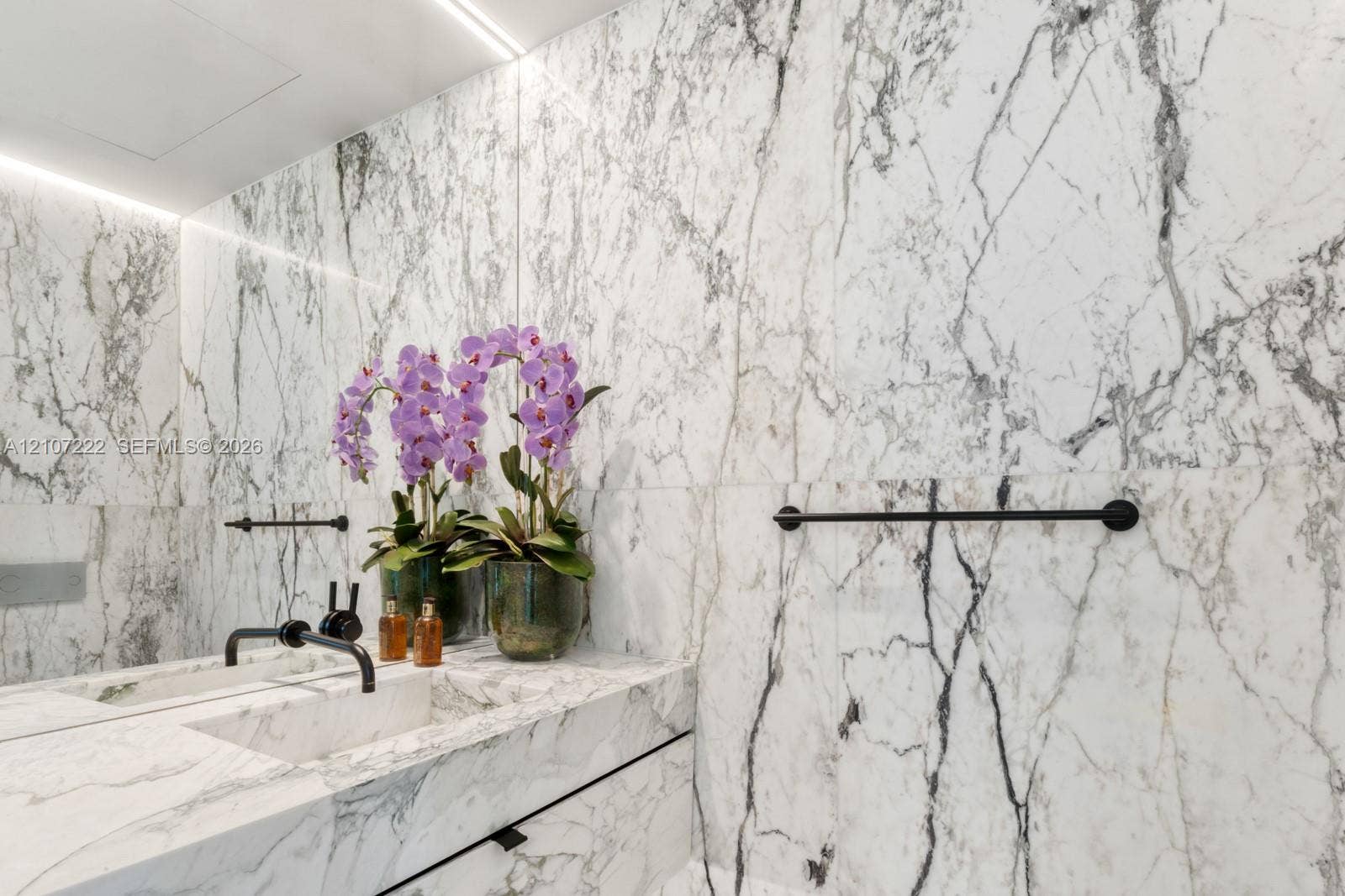 1300 Monad Terrace, #2F, Miami Beach, FL 33139 Full-height stone wall cladding featuring integrated cove lighting, vanity with matching stone countertop, undermount sink, and matte black wall-mounted fixtures