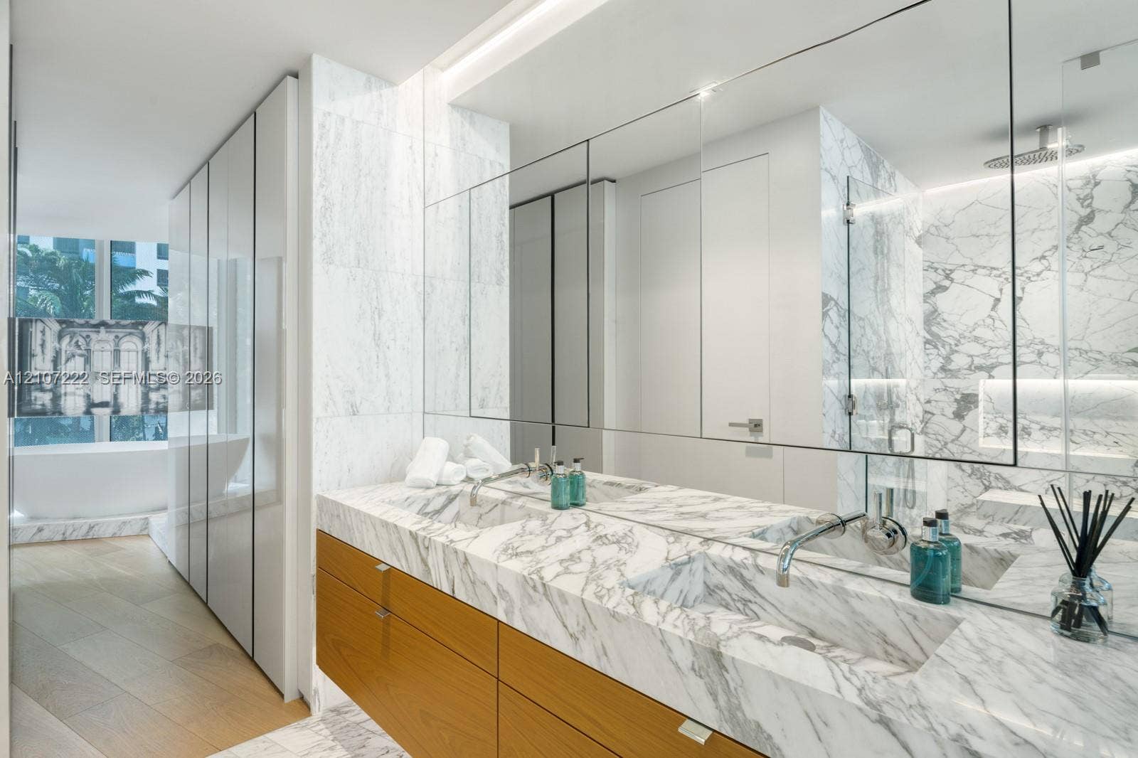 1300 Monad Terrace, #2F, Miami Beach, FL 33139 Double vanity with stone-surfaced integrated sinks and countertop, natural wood-finish cabinetry, floor-to-ceiling stone wall tiling, and glass-enclosed shower area
