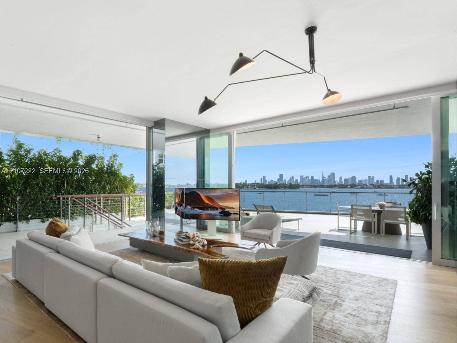 1300 Monad Terrace, #2F, Miami Beach, FL 33139 Open-concept interior featuring floor-to-ceiling glass sliding doors, wood-finish flooring, architectural multi-arm pendant lighting, and a wrap-around balcony with metal railing