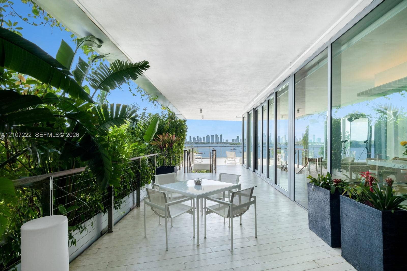 1300 Monad Terrace, #2F, Miami Beach, FL 33139 Covered outdoor terrace featuring light-toned tile flooring, floor-to-ceiling glass panel walls, a stainless steel cable railing system, and integrated built-in planters