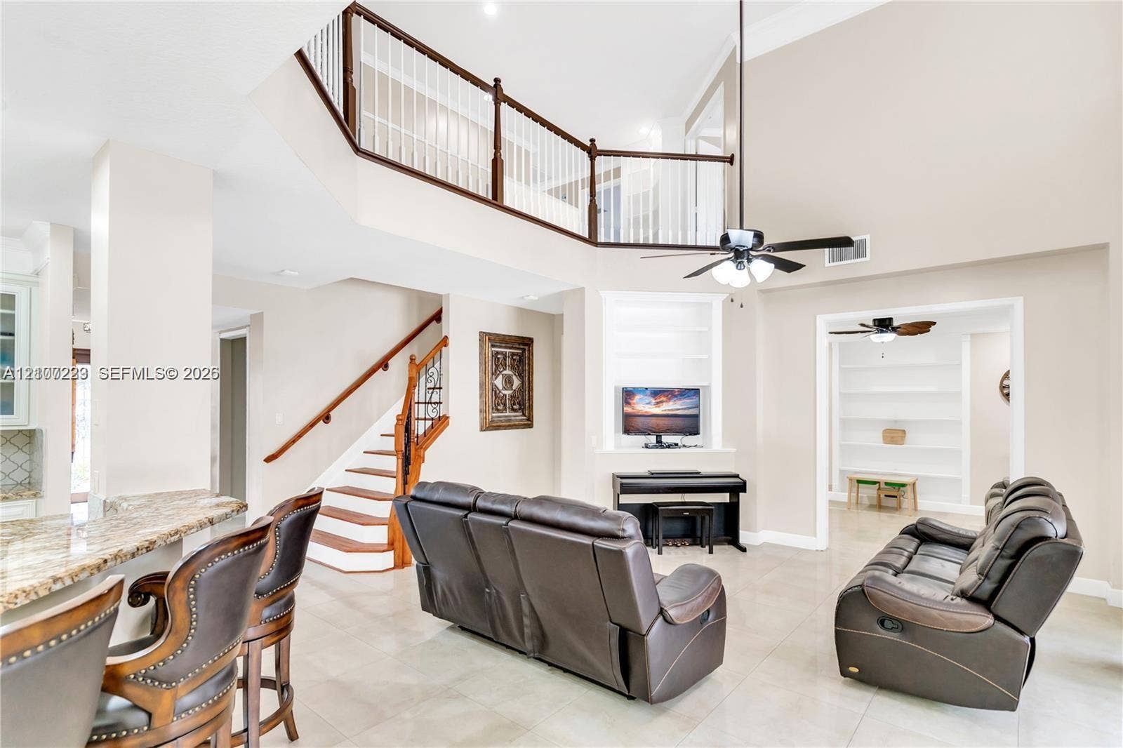 5280 NW 95th Avenue, Coral Springs, Coral Springs, FL 33076 Double-height ceiling, open-railing staircase with wooden handrails, stone-surface breakfast bar, built-in recessed shelving, and large-format tile flooring