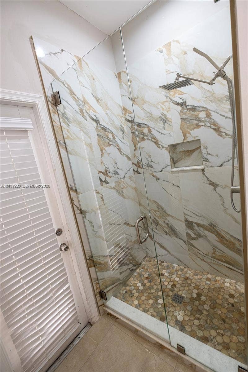 5280 NW 95th Avenue, Coral Springs, Coral Springs, FL 33076 Walk-in shower featuring large-format stone-patterned tile walls, frameless glass enclosure, hexagonal mosaic tile flooring, built-in recessed wall niche, and rainfall shower head with handheld attachment