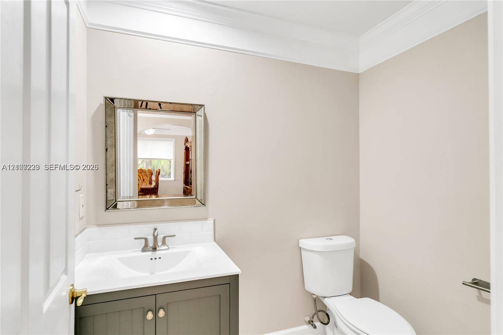 5280 NW 95th Avenue, Coral Springs, Coral Springs, FL 33076 Powder room featuring a shaker-style vanity cabinet, integrated white basin, subway tile backsplash, crown molding, and a decorative beveled-edge wall mirror