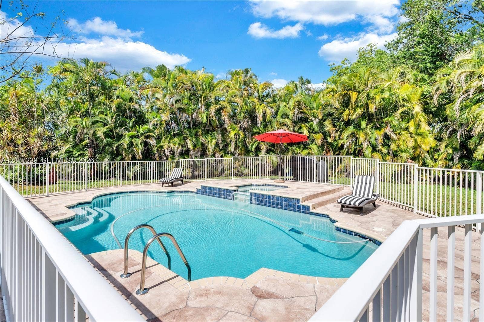 5280 NW 95th Avenue, Coral Springs, Coral Springs, FL 33076 Swimming pool with raised spa, stone-textured pool deck, and metal perimeter fencing surrounded by dense mature vegetation
