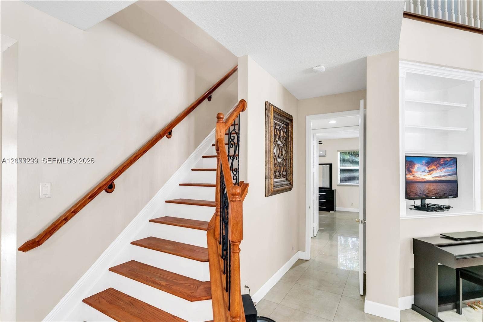 5280 NW 95th Avenue, Coral Springs, Coral Springs, FL 33076 Staircase featuring wood-finish treads, a wood handrail, and wrought-iron balusters, accompanied by built-in shelving with recessed lighting and large-format tile flooring