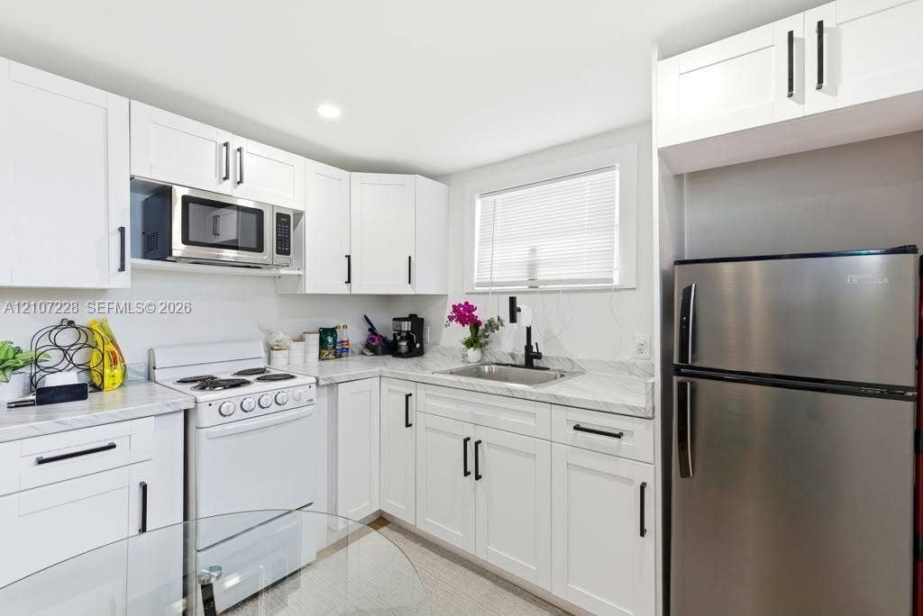Kitchen featuring white Shaker-style cabinetry, stone-patterned countertops, stainless steel appliances, and a matte black gooseneck faucet
