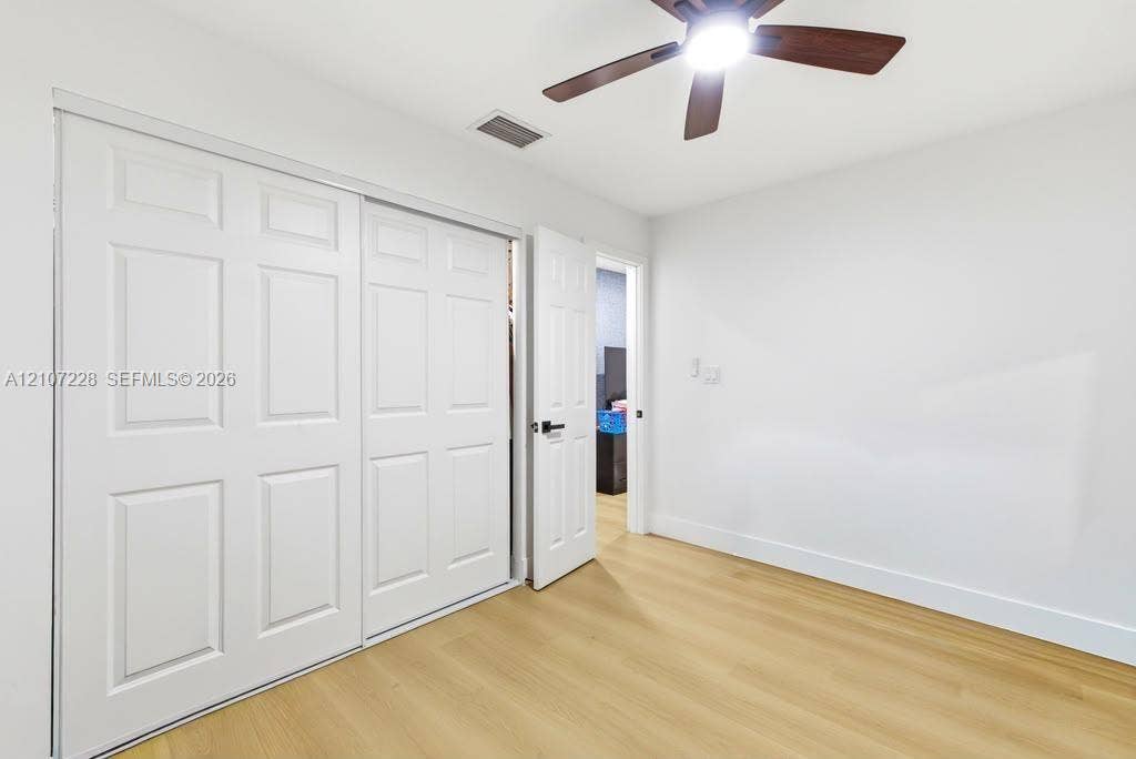 Room featuring wood-finish flooring, white six-panel sliding closet doors, a matching six-panel hinged door, and a ceiling fan with integrated lighting